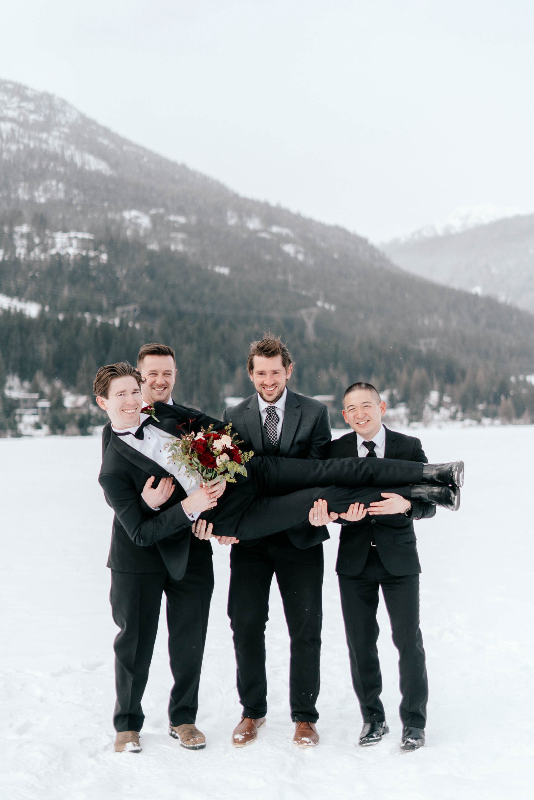 Silly groomens hold the groom up in the air as they pose for the camera in the snowy mountains of Whistler, BC. 