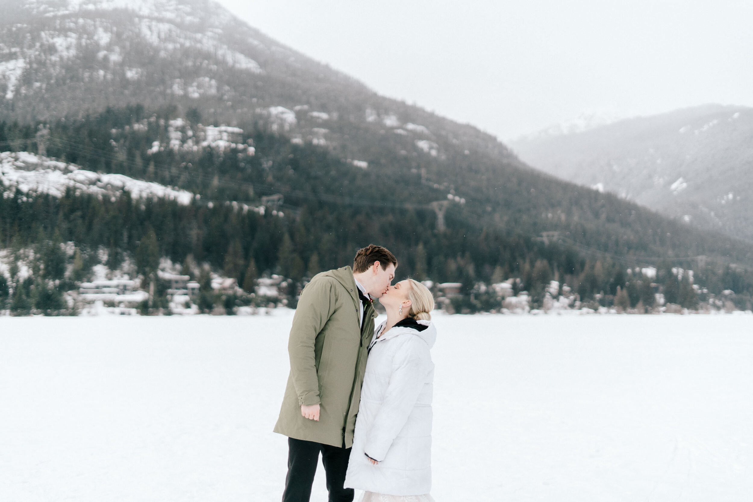 A bride and groom kiss while wearing winter jackets in Whistler, BC.