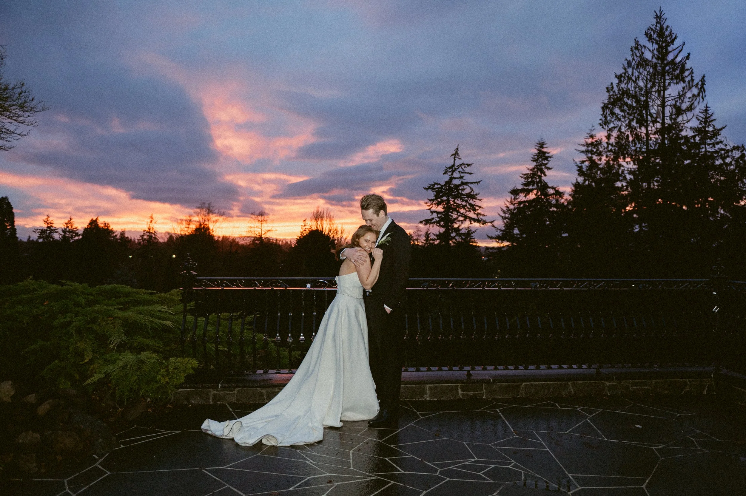 Bride and groom embracing at sunset on an outdoor terrace.