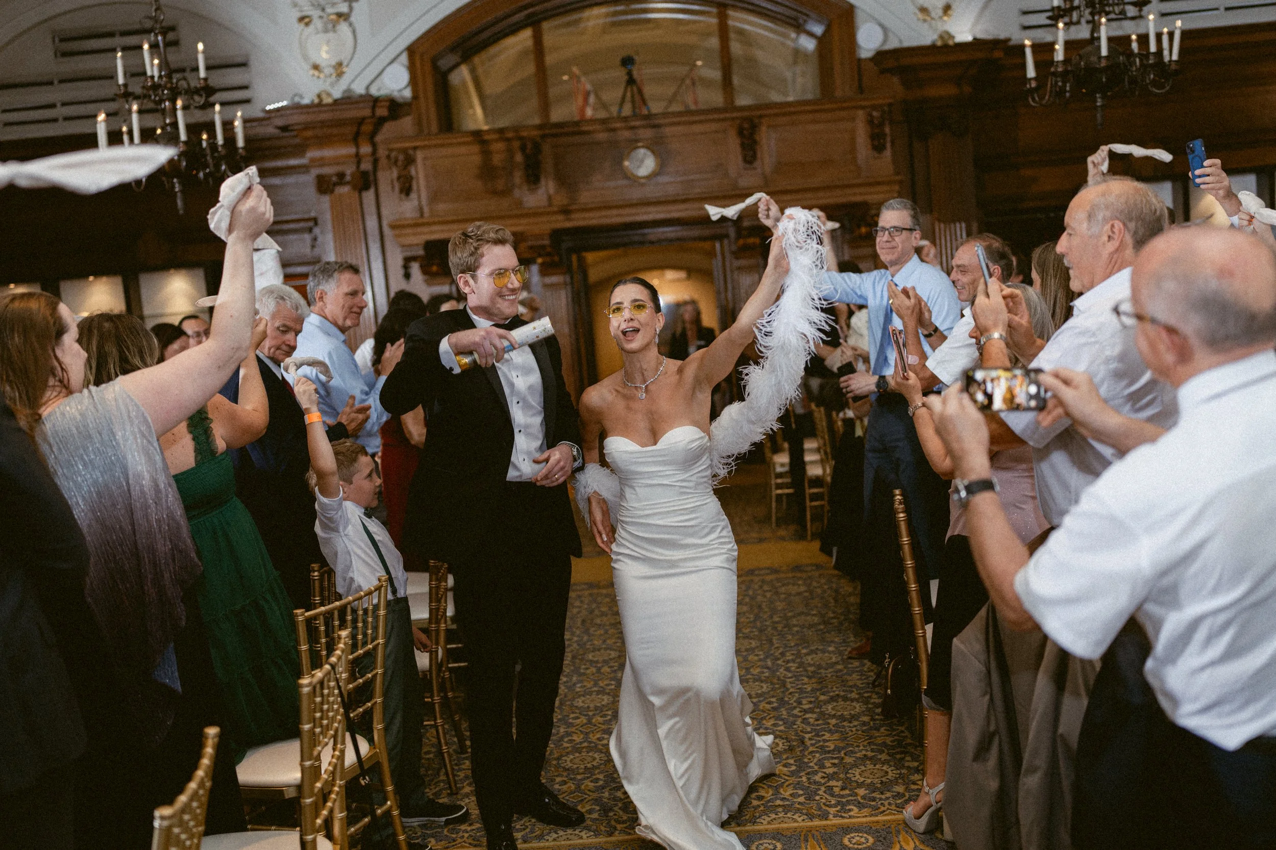 Wedding reception at the Vancouver Club, with the newlyweds making a joyful grand entrance as guests cheer and wave napkins inside the historic Vancouver Club ballroom.