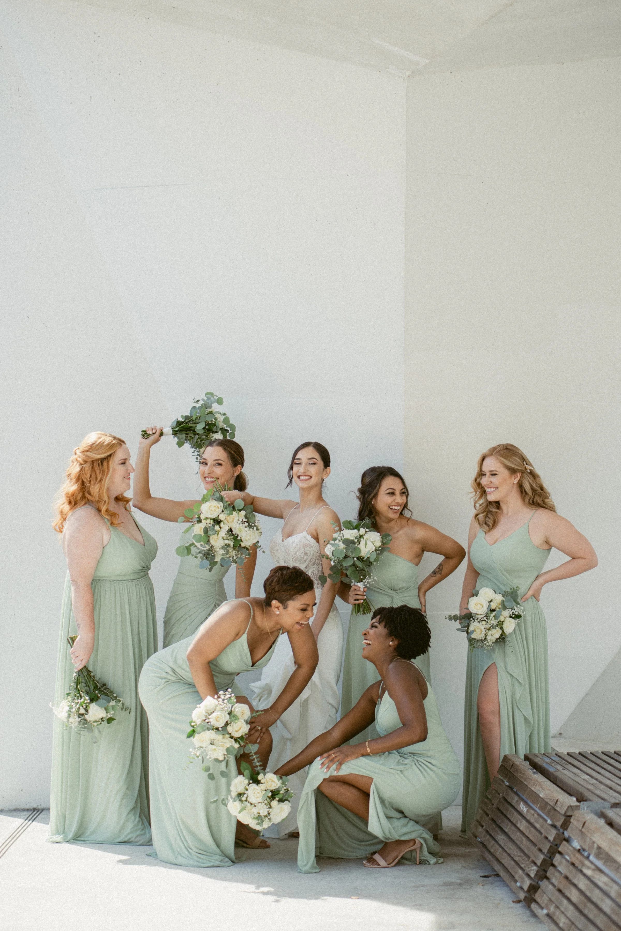 Bride laughing with her bridesmaids in sage green dresses at UBC.