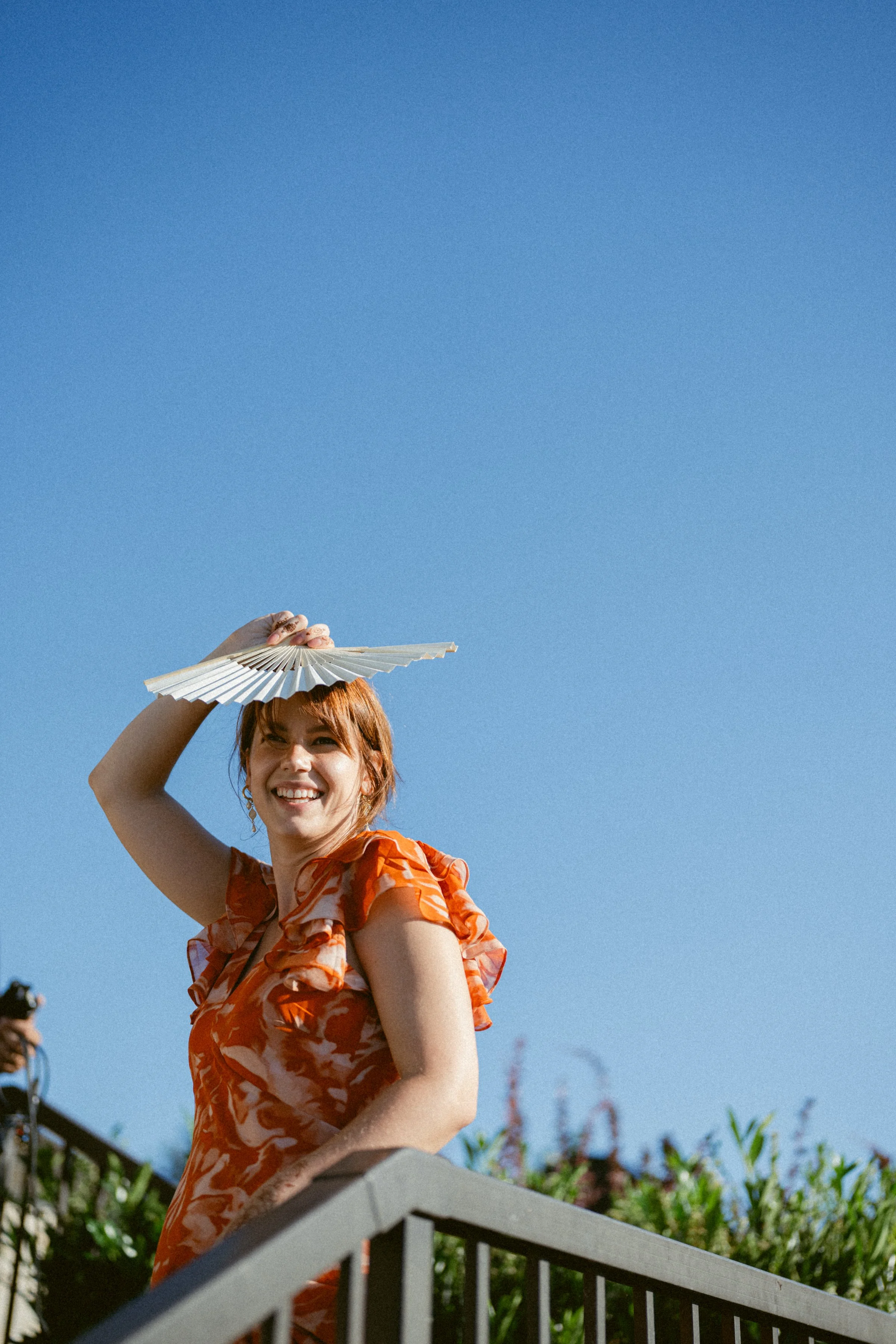 Guest during cocktail hour wearing a bright red dress with blue sky in the background.