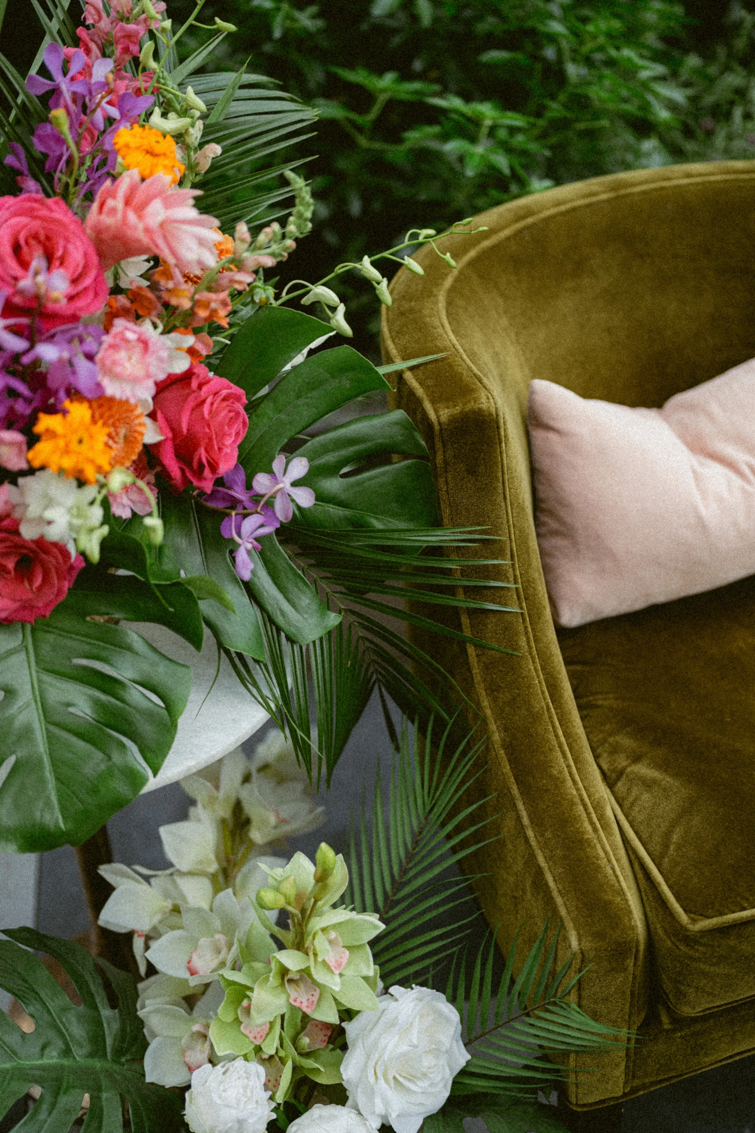 Vibrant wedding florals styled beside a velvet chair.