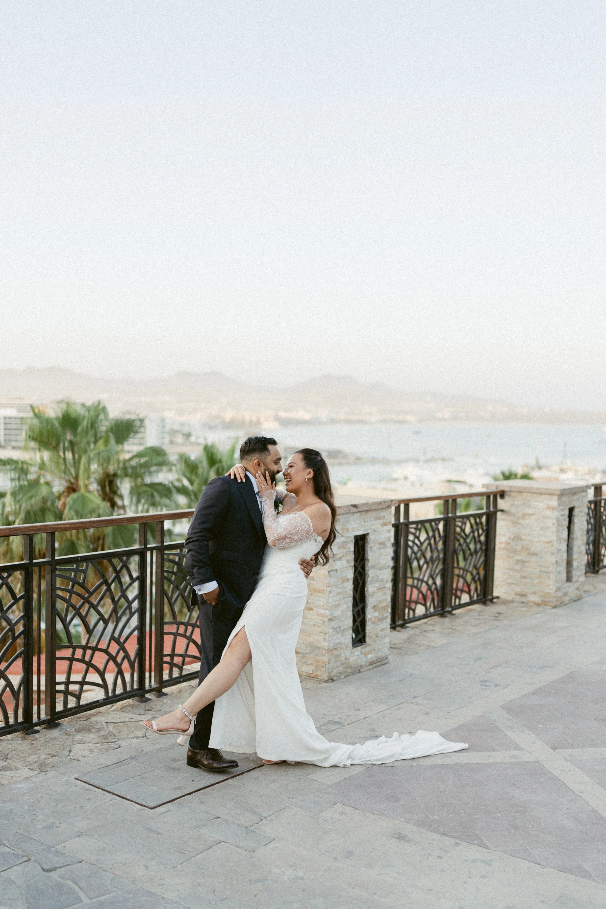 Bride and groom laughing together on a terrace overlooking the ocean in Mexico.