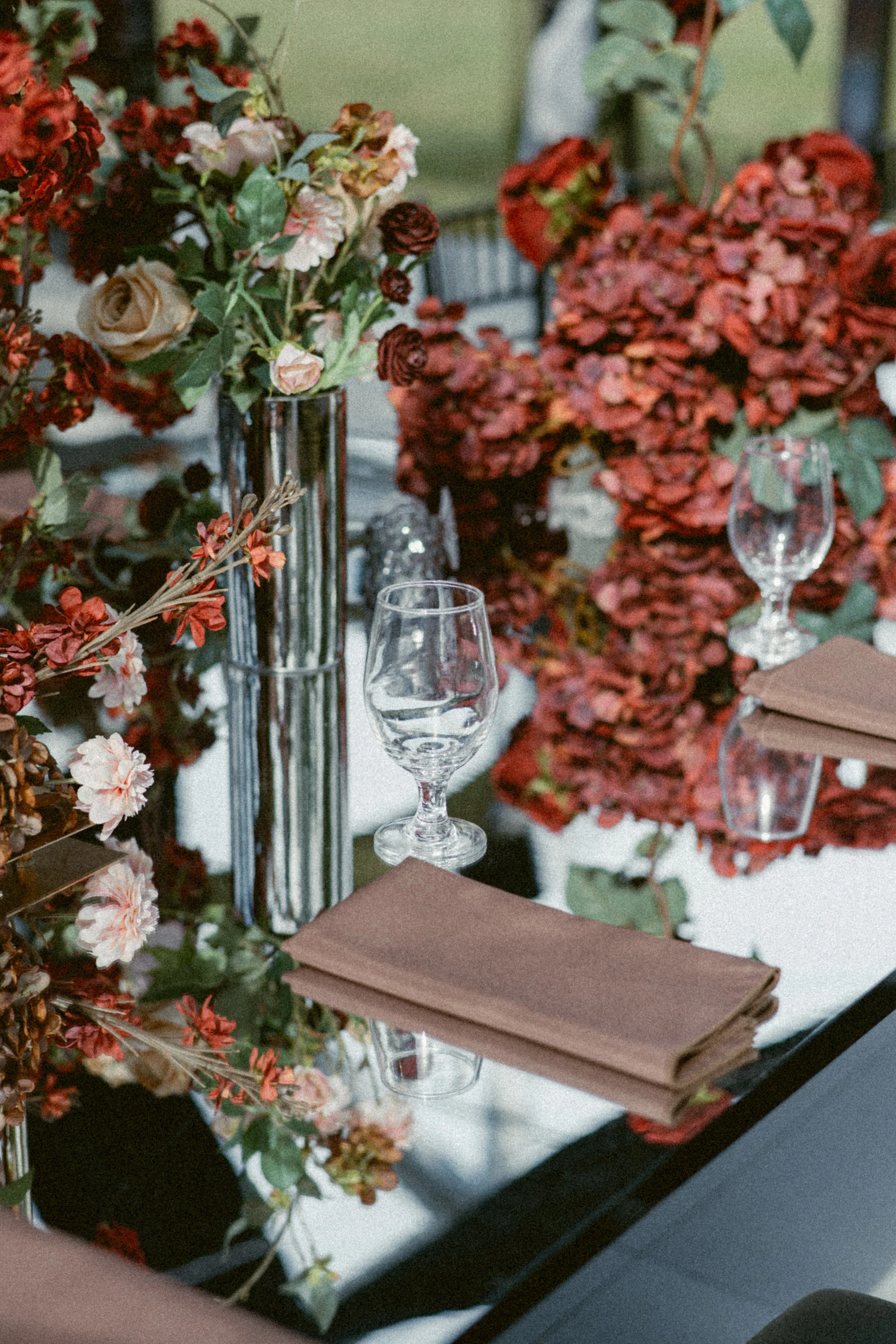 Moody tablescape with red floral arrangements, glassware, and folded napkins styled for a modern wedding reception.