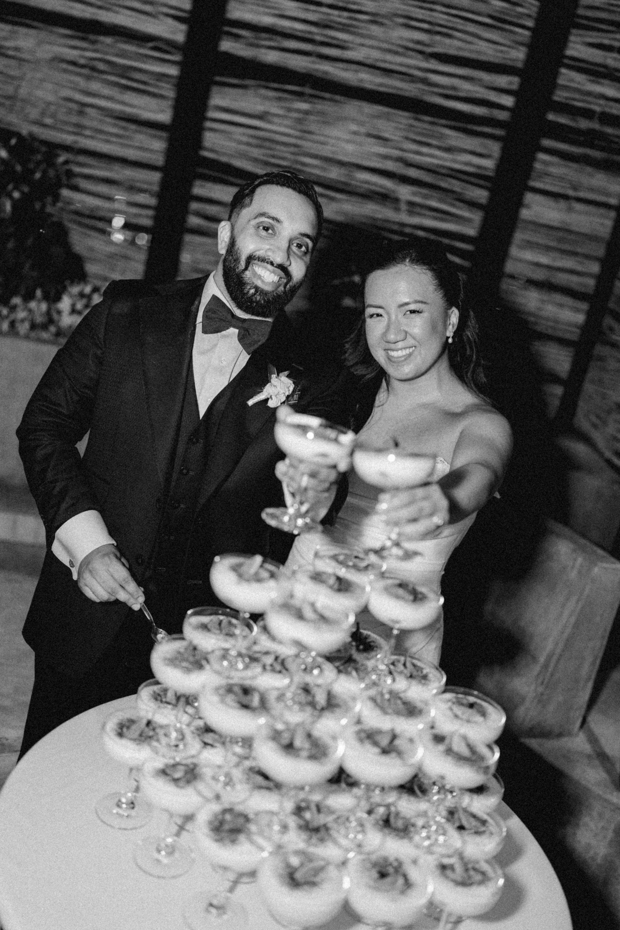 Black and white image of wedding couple making a cheers with dessert filled champagne coupe glasses in Mexico.