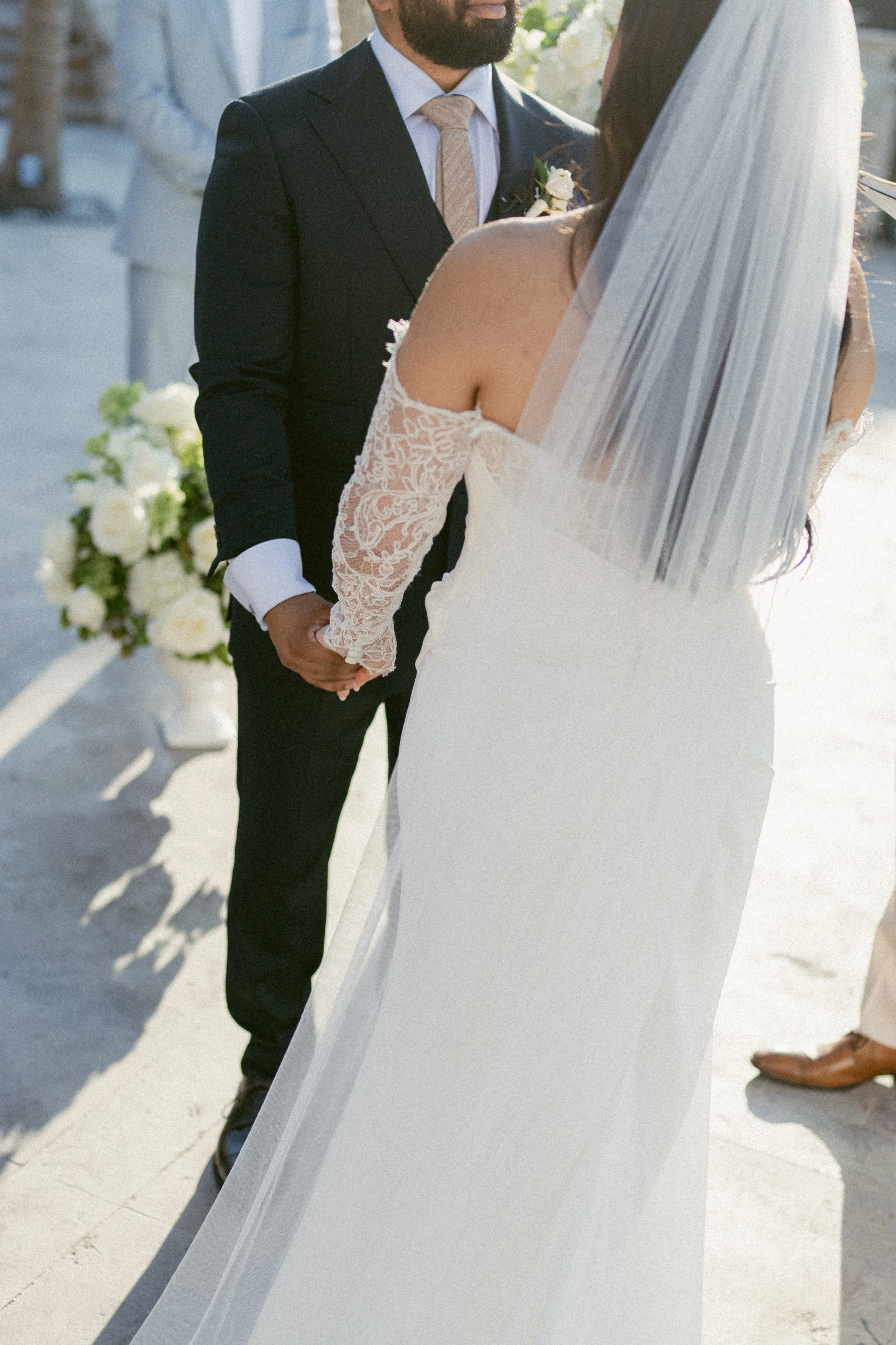 Close-up of bride and groom holding hands during a sunlit ceremony in Mexico.