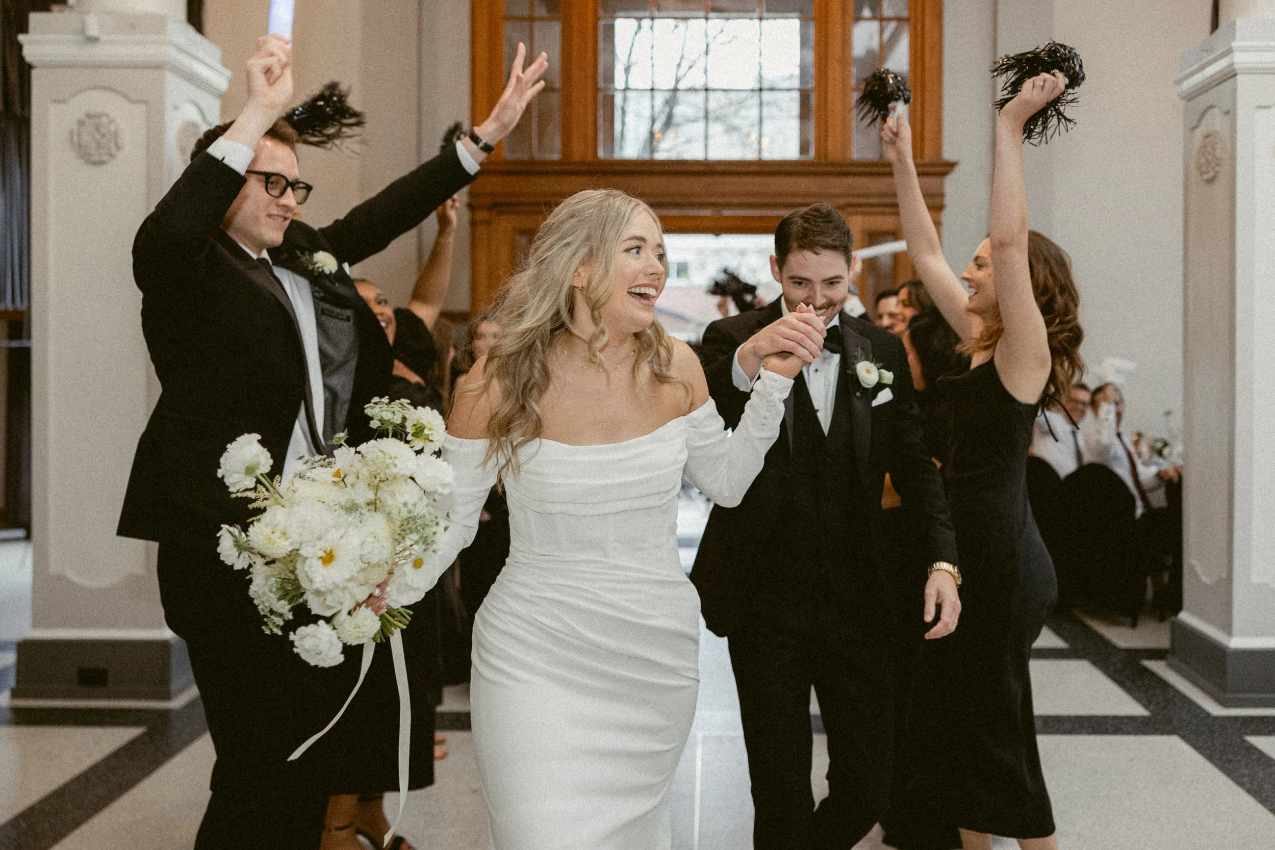Joyful wedding exit moment with the bride and groom holding hands and smiling as guests cheer behind them.