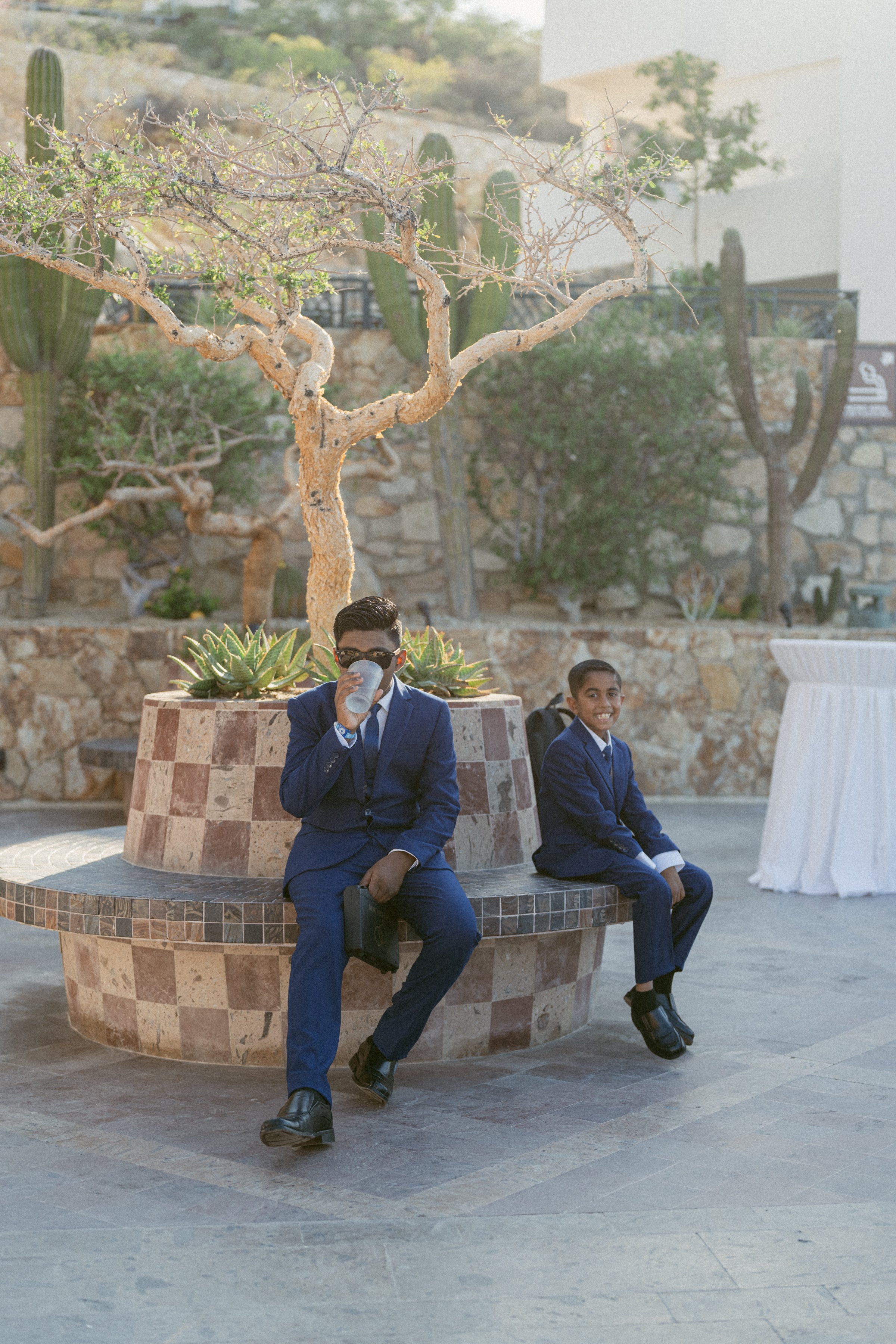 Two boys in navy suits sitting together during a wedding celebration.