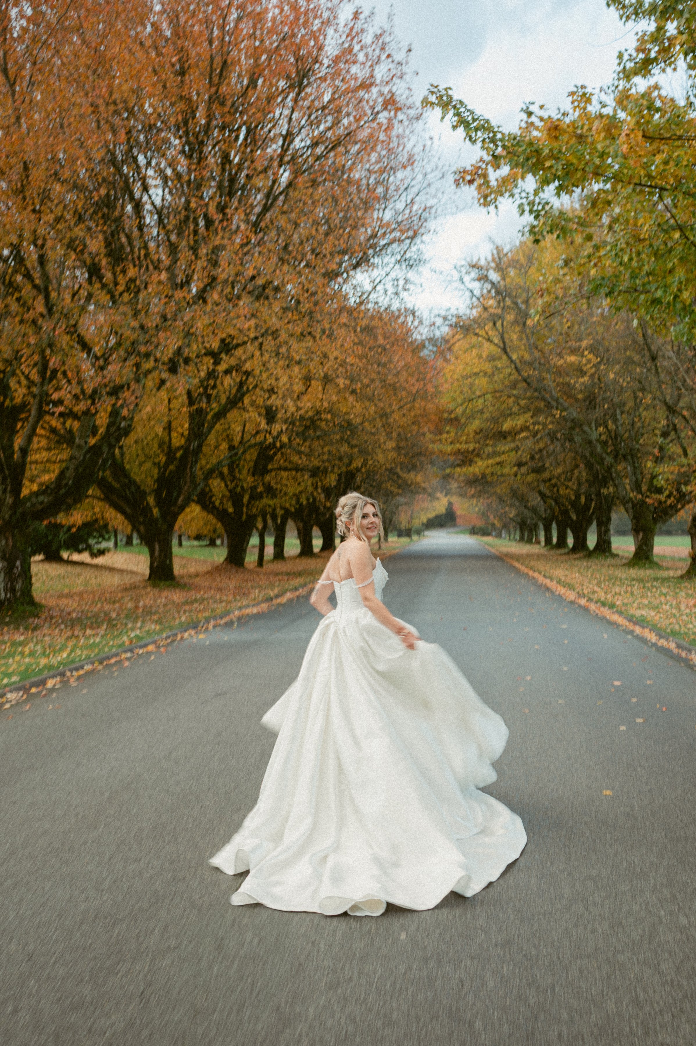 Bride running in her gown on a tree-lined road with fall colours at Swaneset Bay Resort.