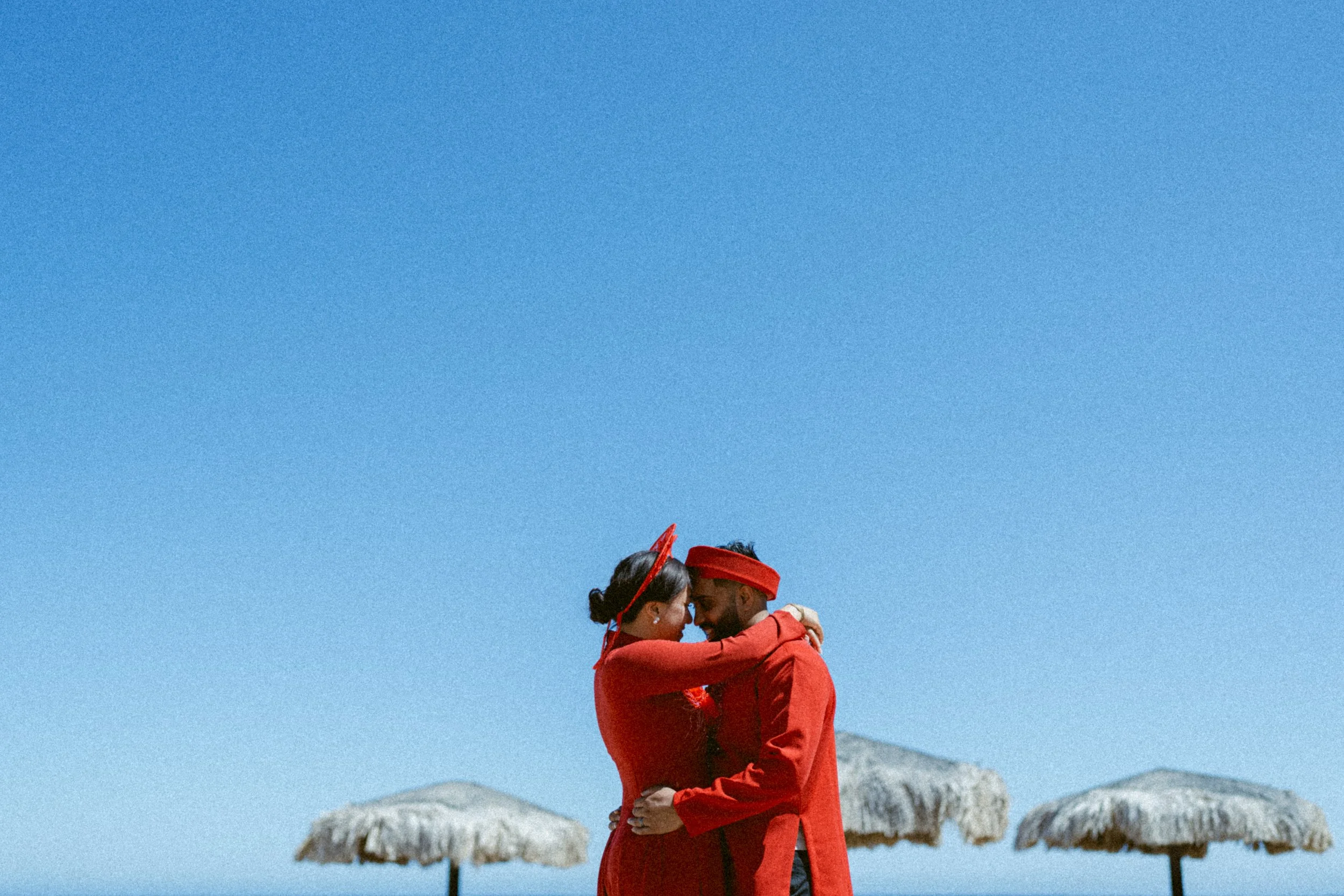 Couple embracing in coordinated red outfits against a clear blue sky in Mexico.
