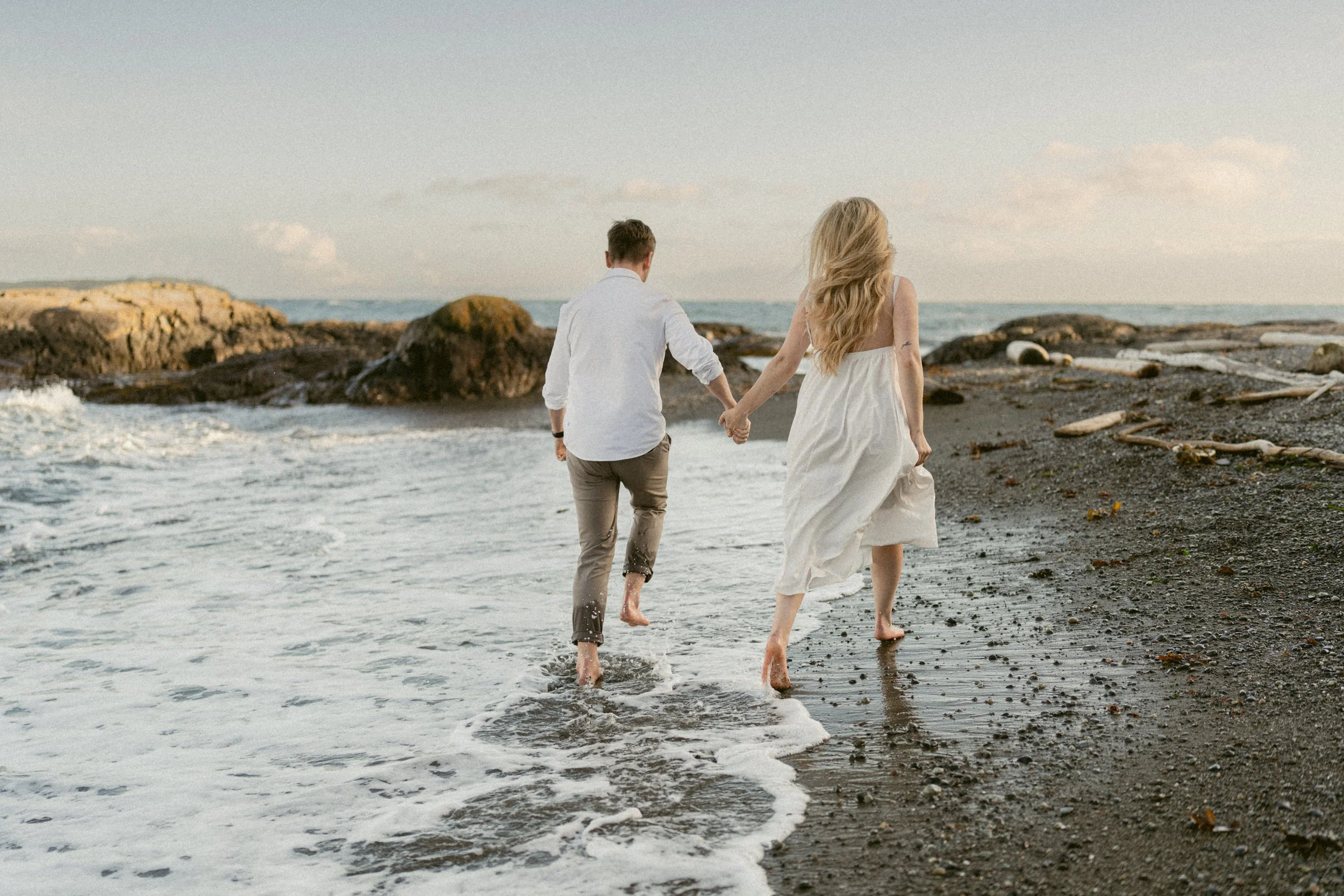 Couple running barefoot through the waves during a Vancouver Island engagement session.