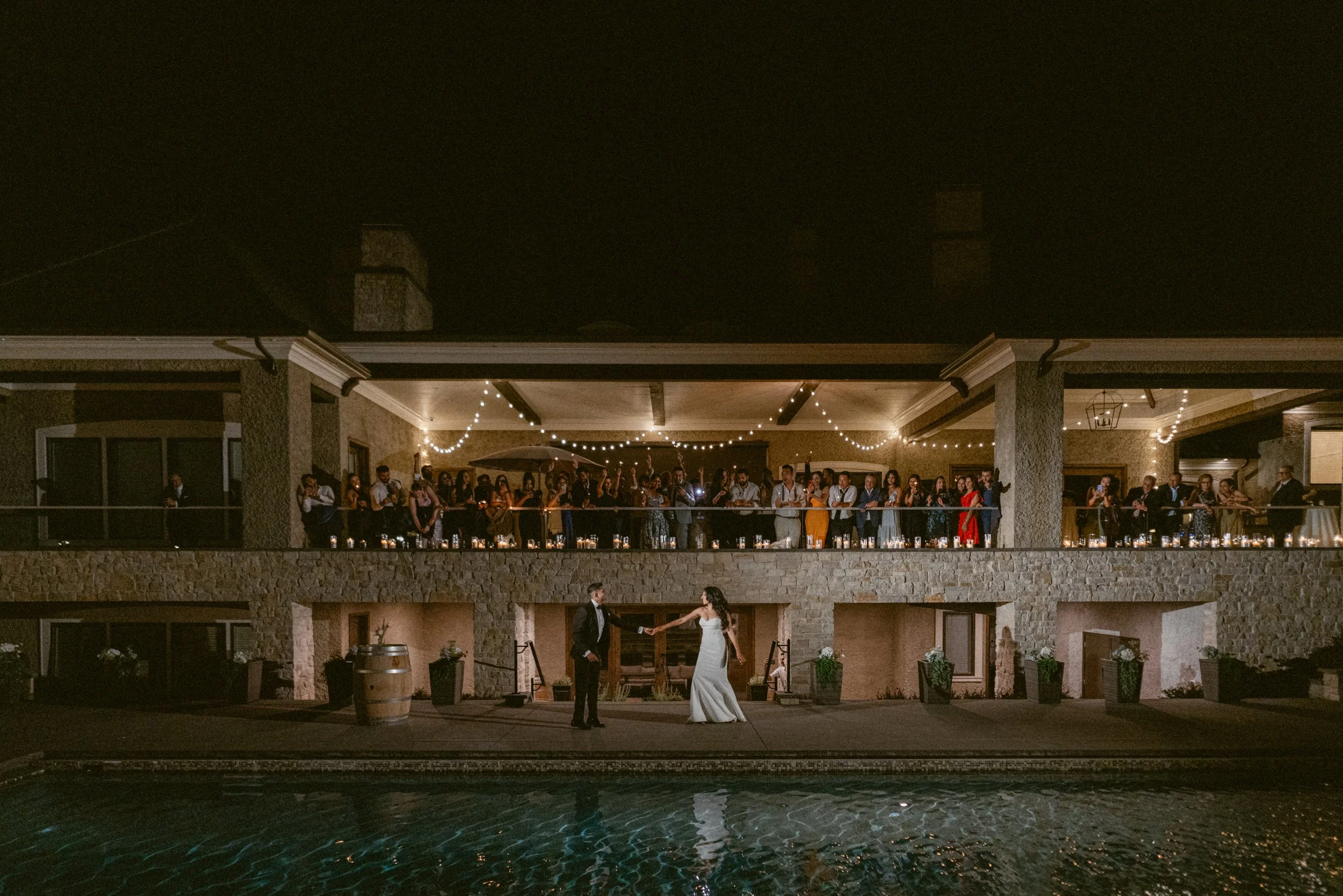 Bride and Groom first dance outside house under lights as guests watch from the balcony.