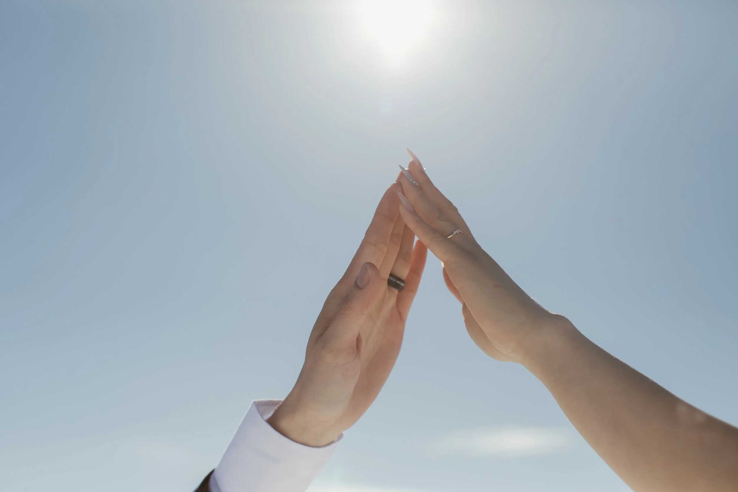 Wedding rings touching hands against the sky during a mountain helicopter session.