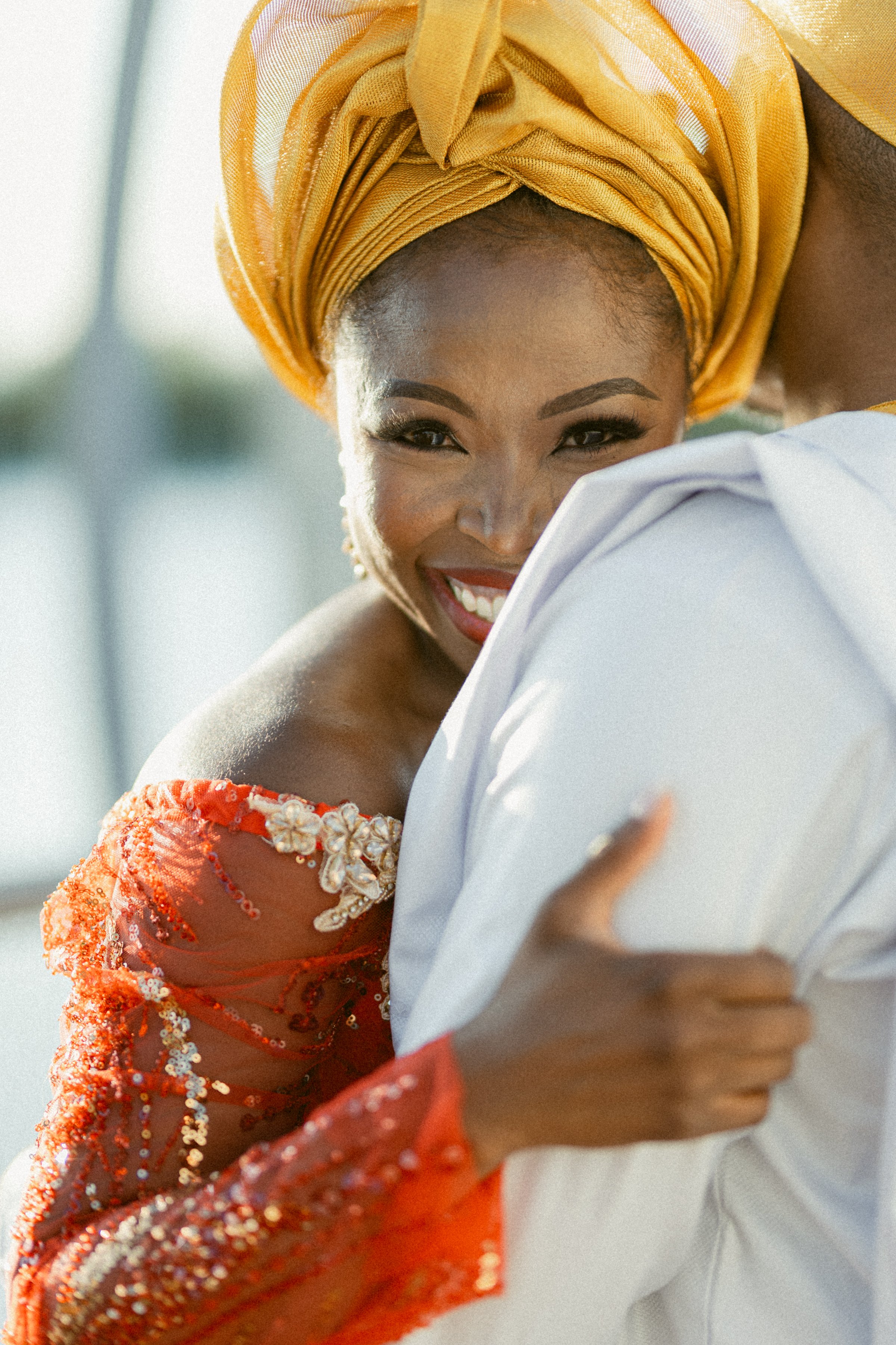 Bride smiling during an intimate embrace with her partner at the UBC Boathouse, wearing vibrant red and gold traditional wedding attire.