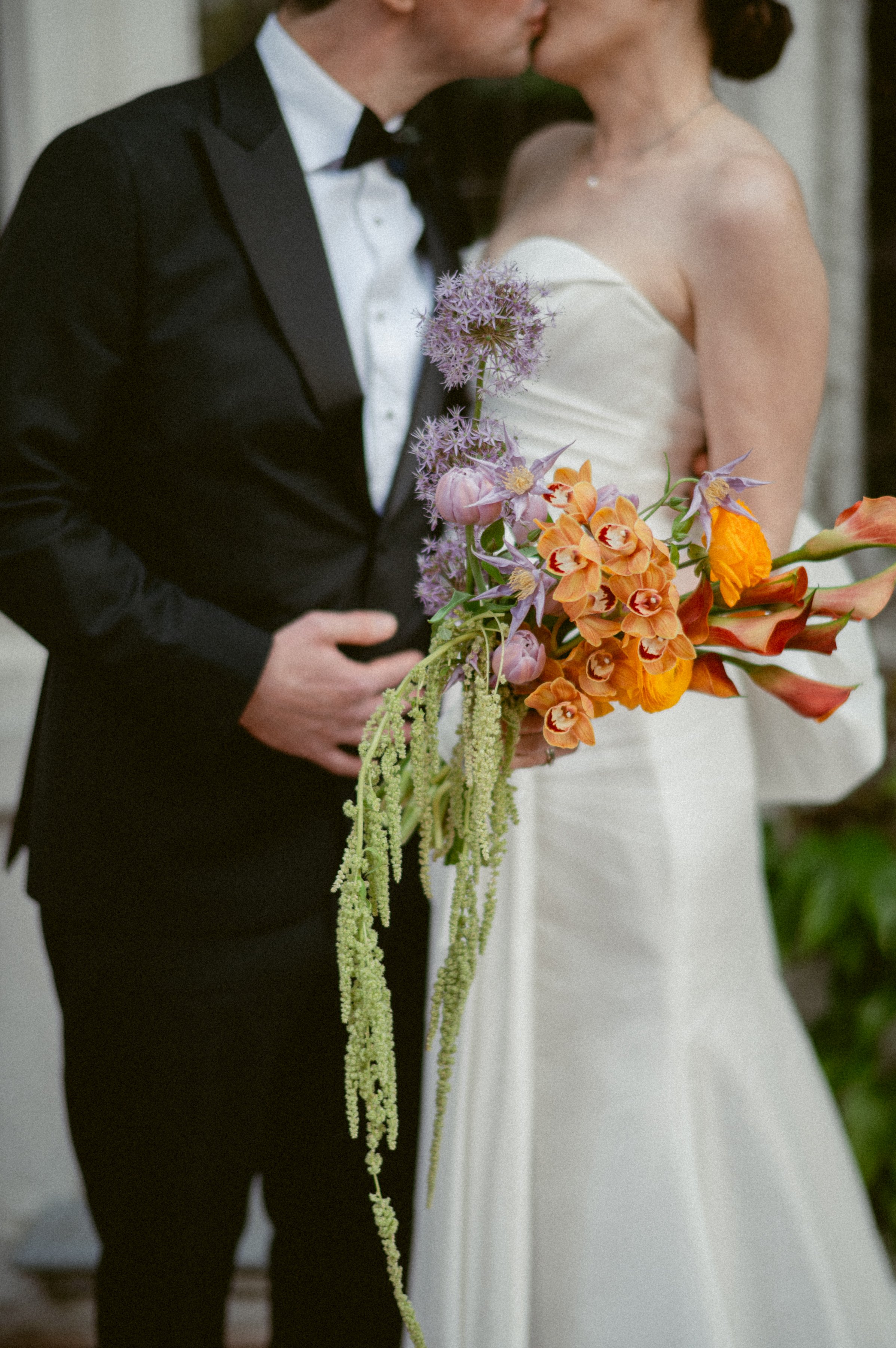 Bride and groom kissing behind a colorful wedding bouquet.