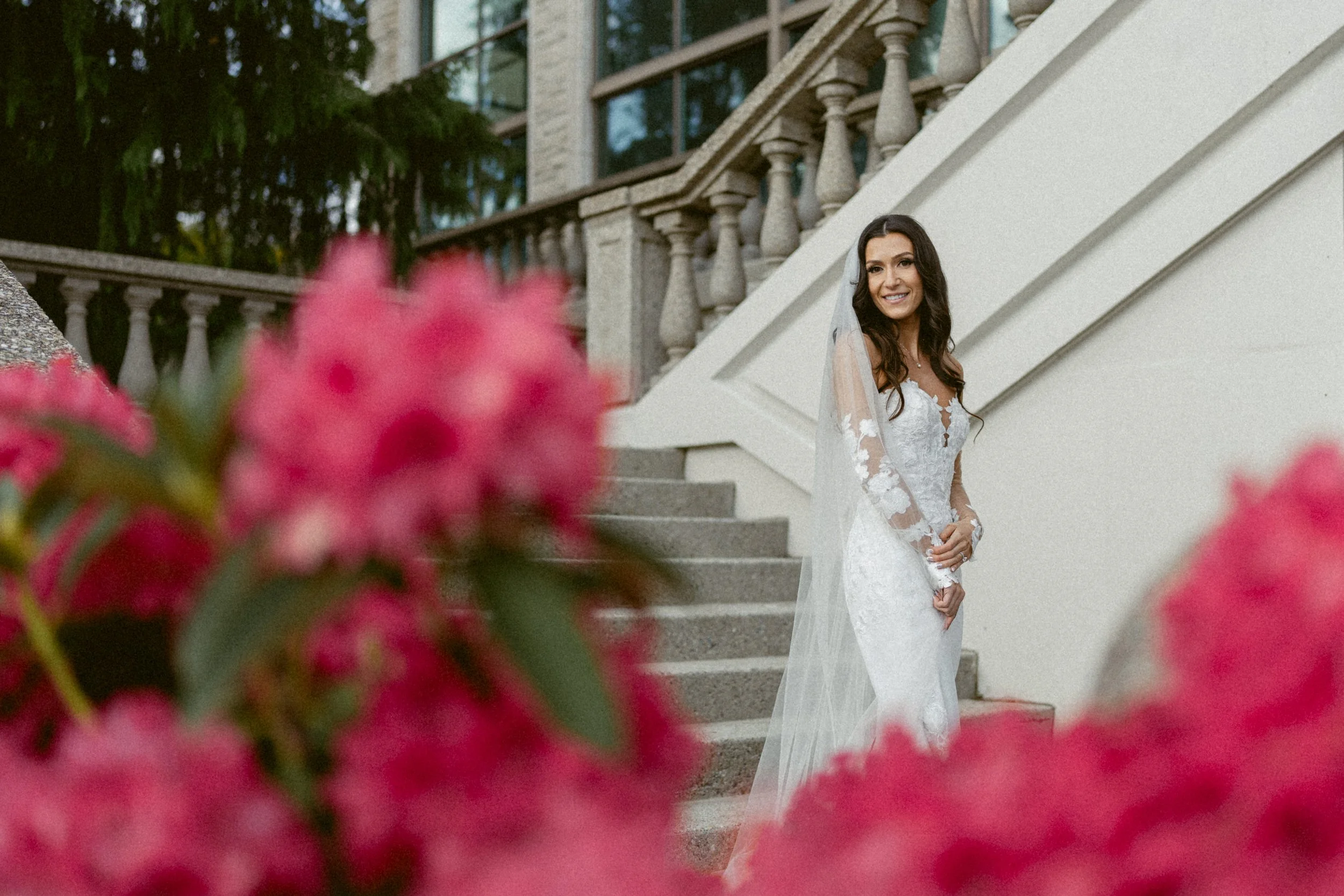 Bride standing on stone steps framed by soft pink flowers at Swaneset Bay Resort.