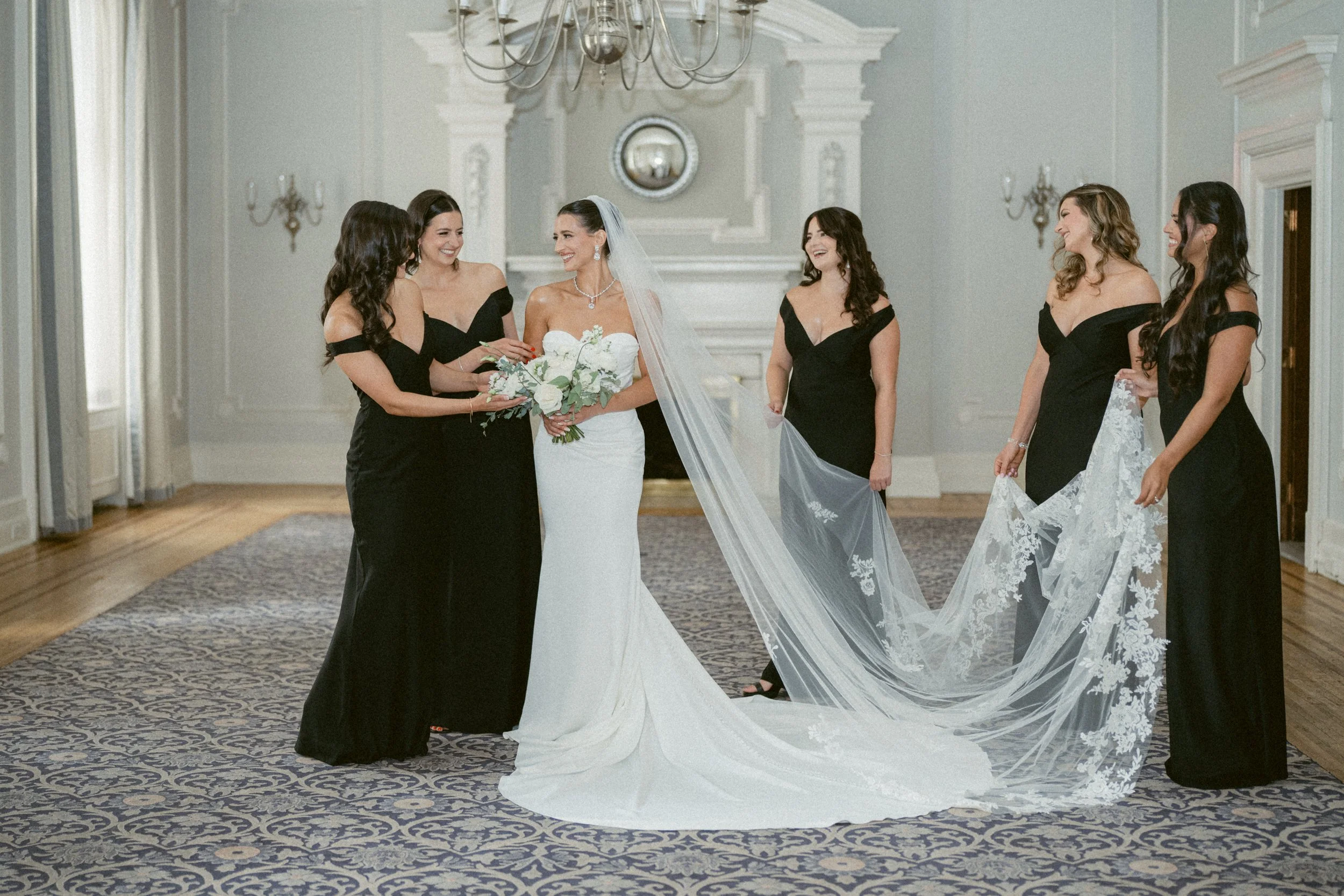 Bride sharing a moment with bridesmaids while holding her veil indoors at the Vancouver Club.