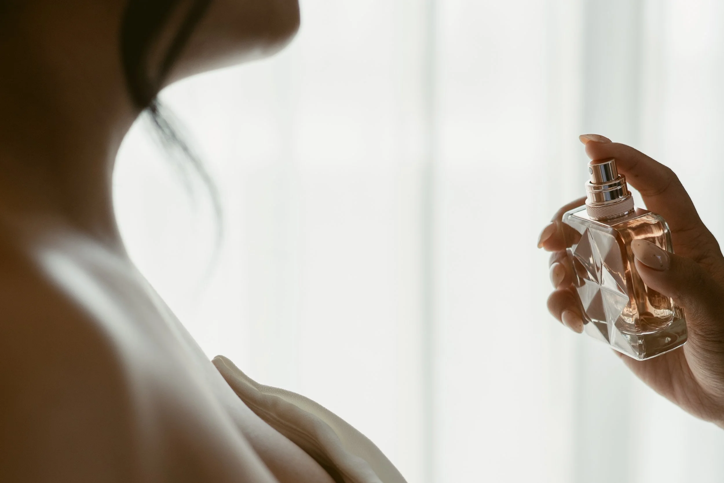Close-up detail of a bride holding a glass perfume bottle, captured in soft window light during getting ready.