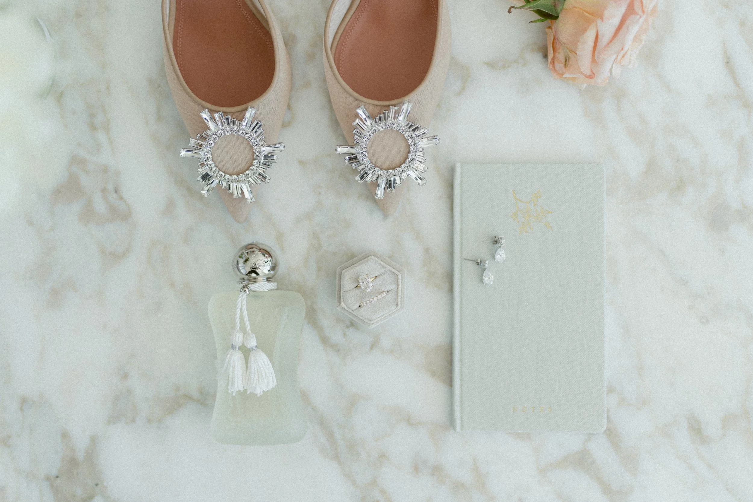 Bridal accessories flat lay with embellished heels, perfume, rings, and earrings.