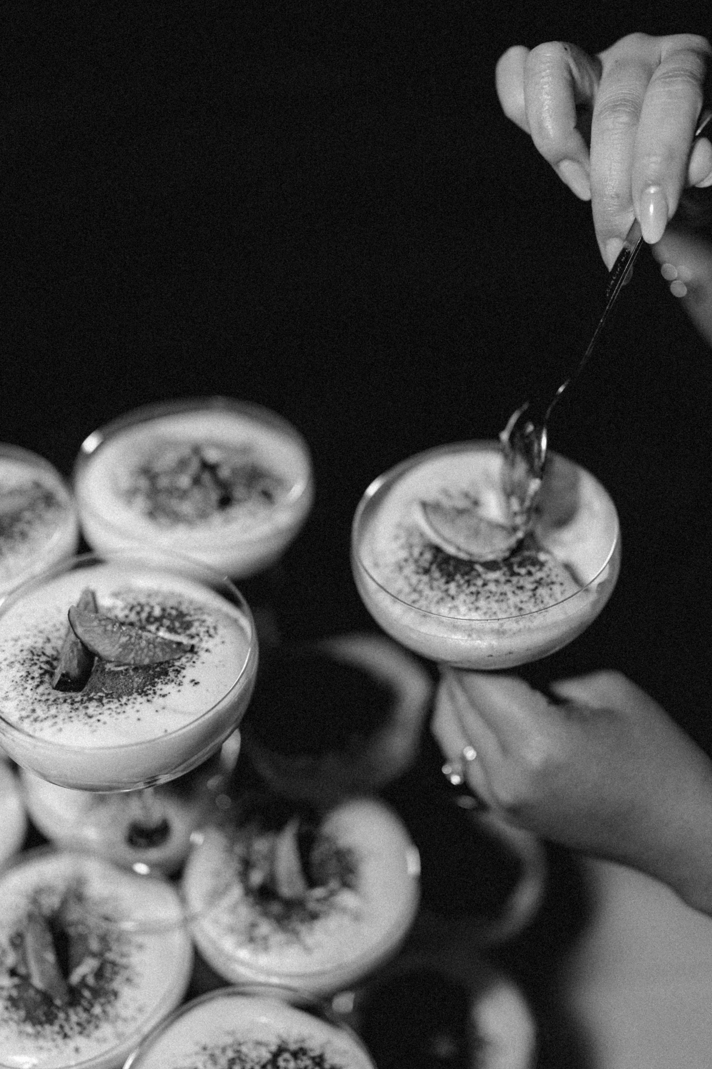 Black and white close-up of hands holding a spoon while eating elegant dessert.
