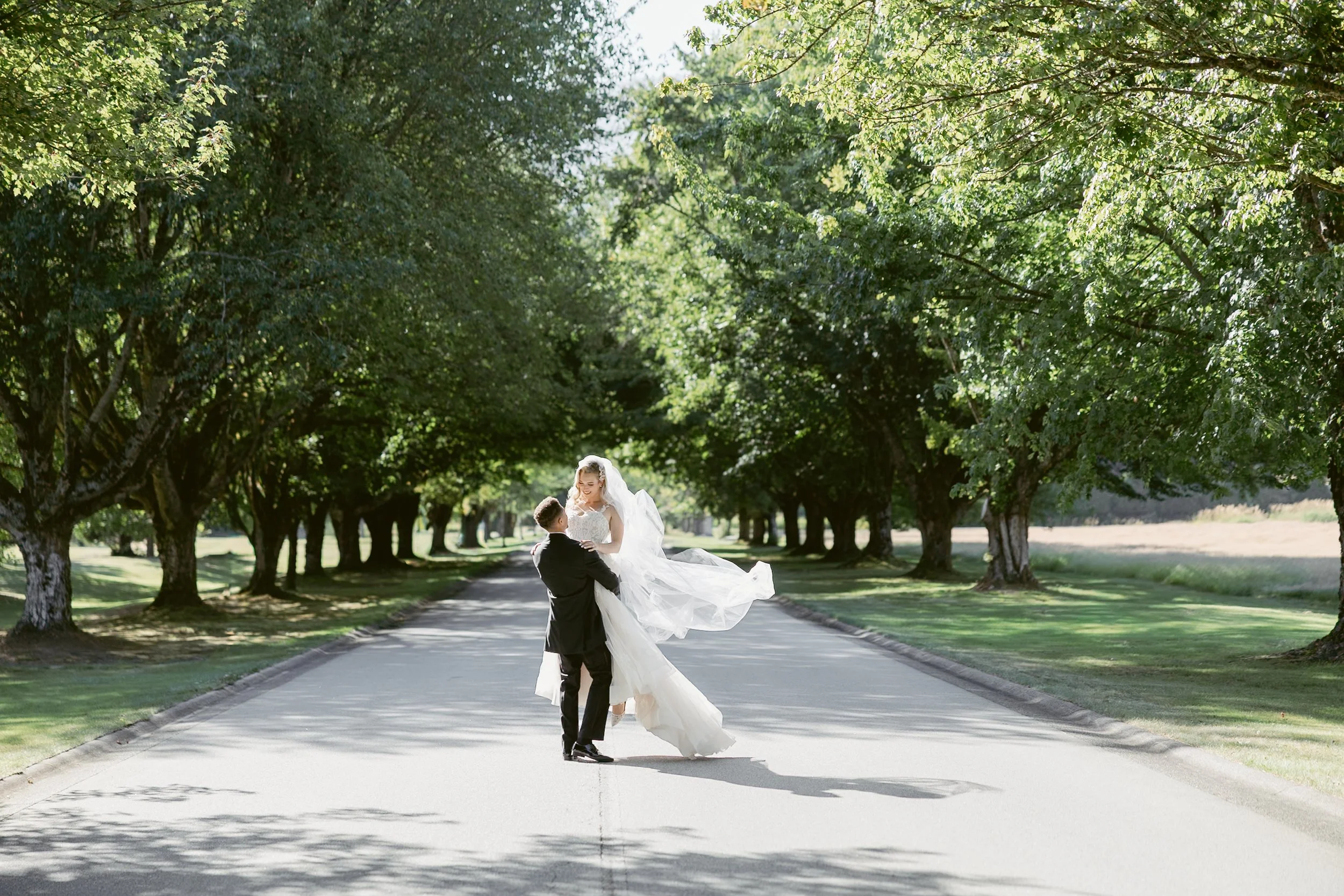 Bride and groom share a joyful moment as the groom lifts the bride in the middle of a tree-lined road at Swaeset Bay Resort.