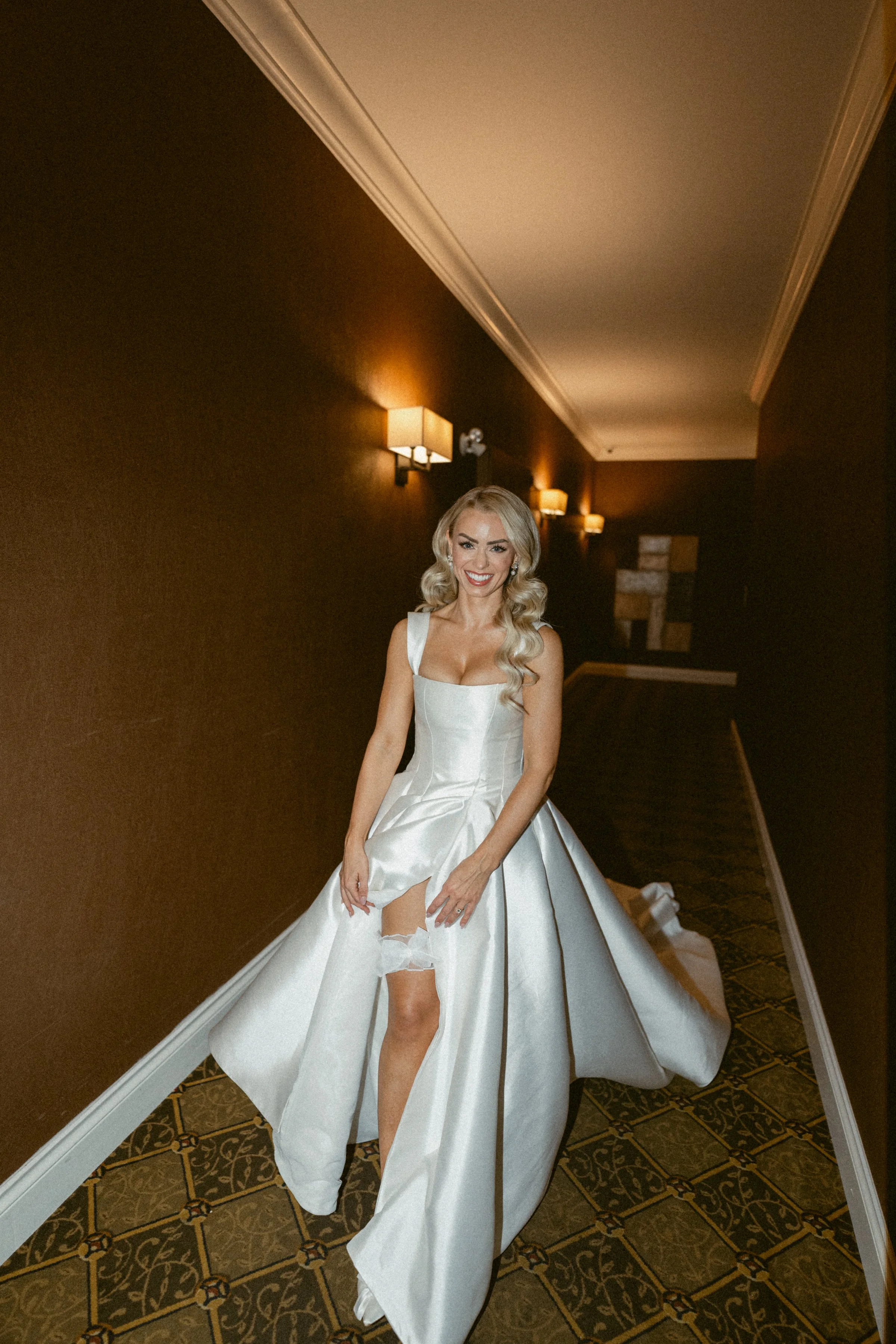 Bride walks down a hallway while adjusting her garter.