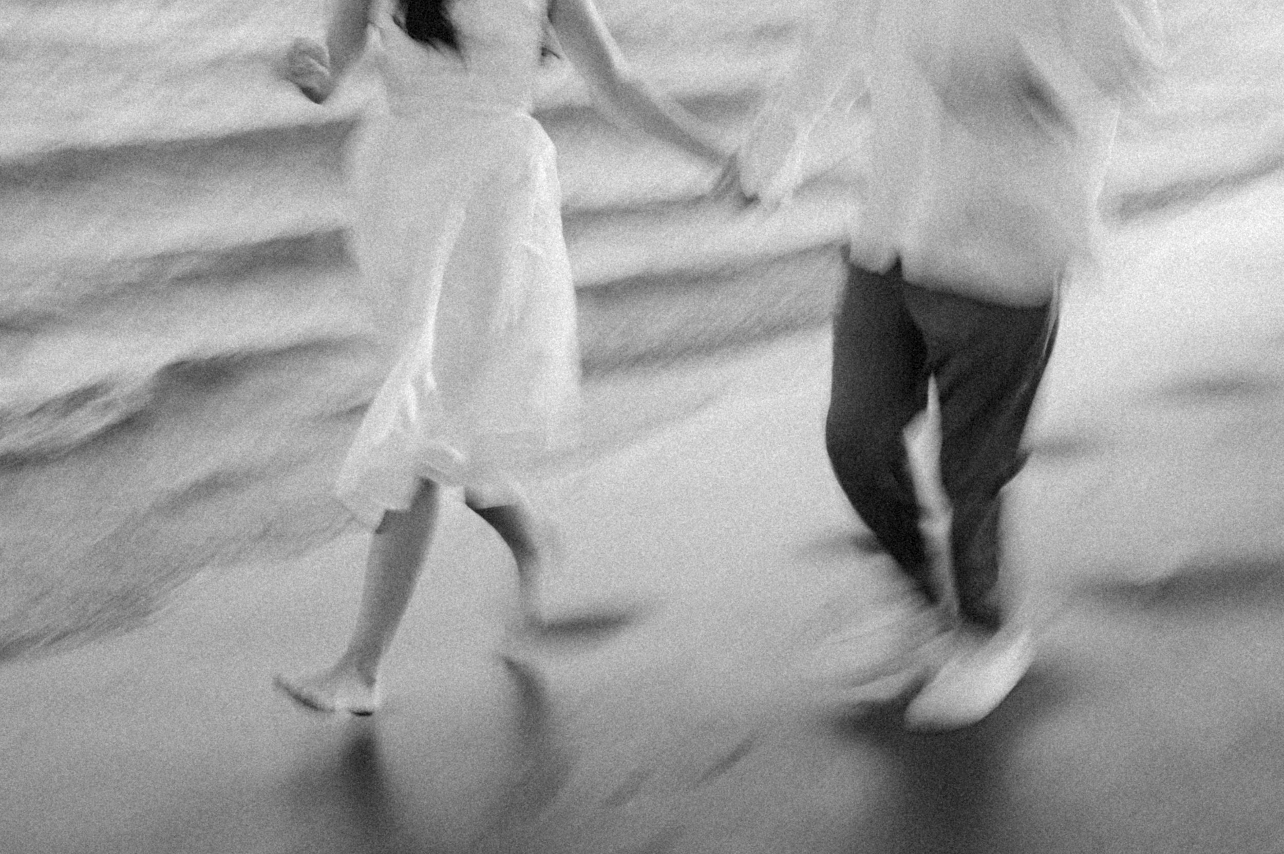 Artistic black and white engagement photo with movement on the beach.