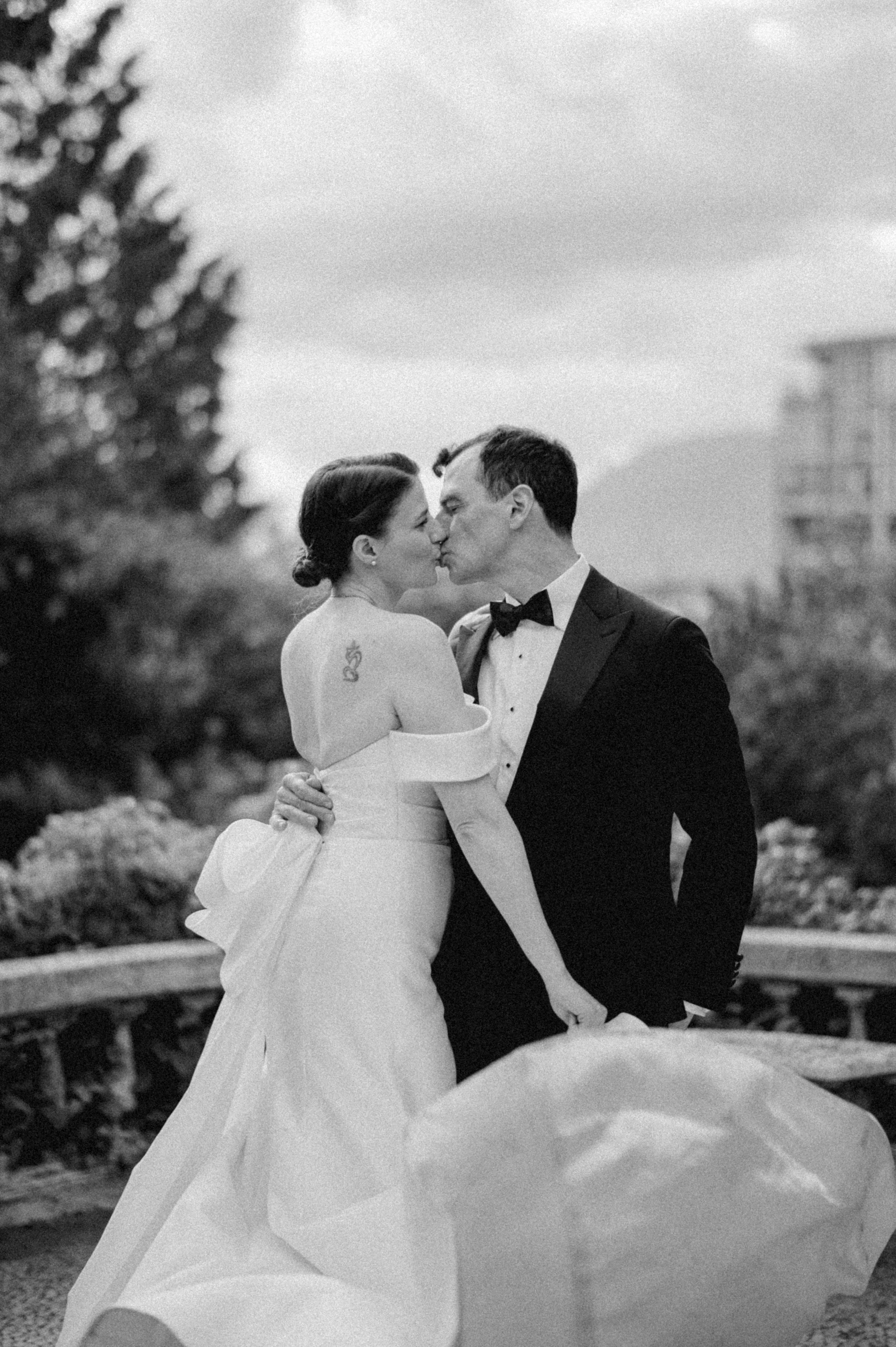 Black and white portrait of a bride and groom sharing a kiss outdoors.