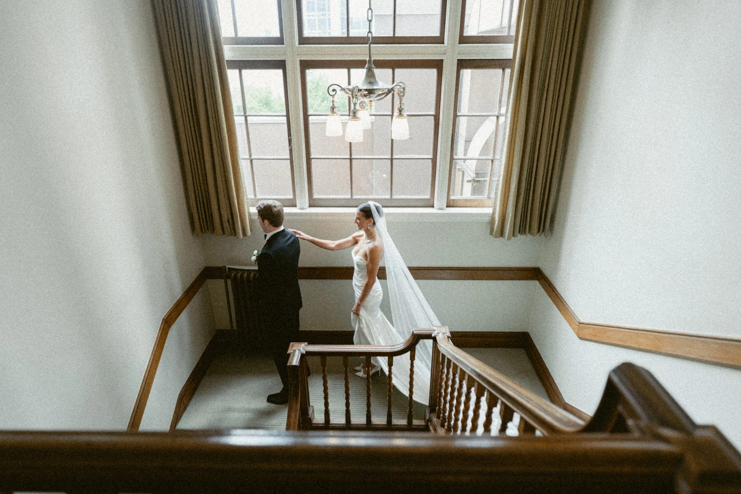 Bride taps groom on the shoulder for a first look on a grand staircase at Vancouver Club.