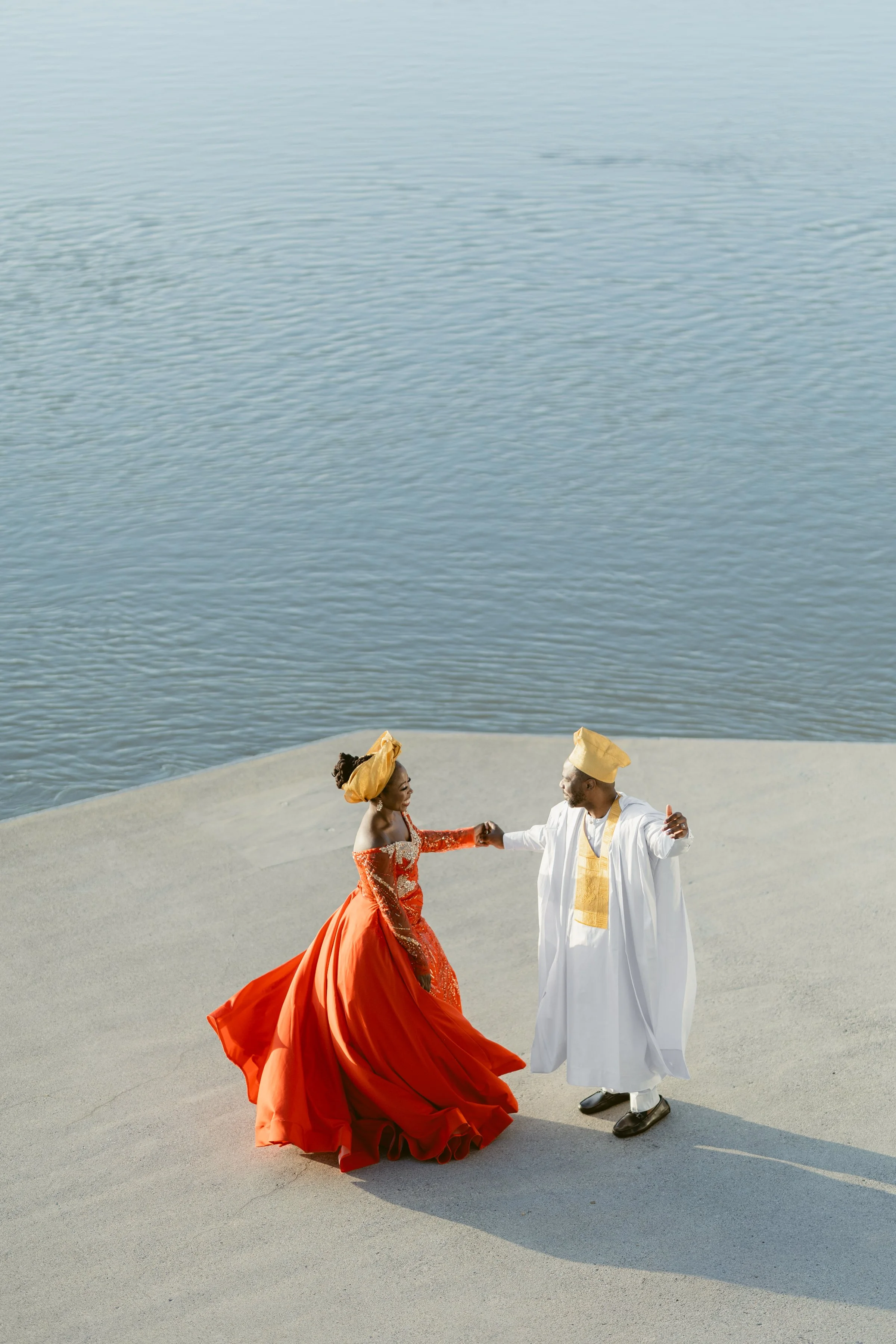 Bride and Groom dancing on cement surrounded by water at UBC Boathouse wearing traditional African wedding attire in red, white and gold.