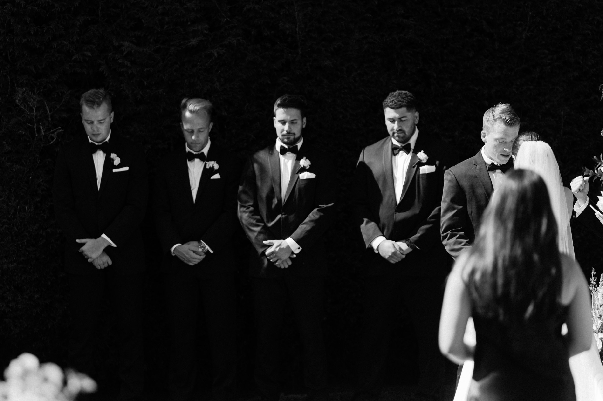 Black and white wedding ceremony in the Okanagan featuring the groom and groomsmen standing at the altar as the bride approaches.