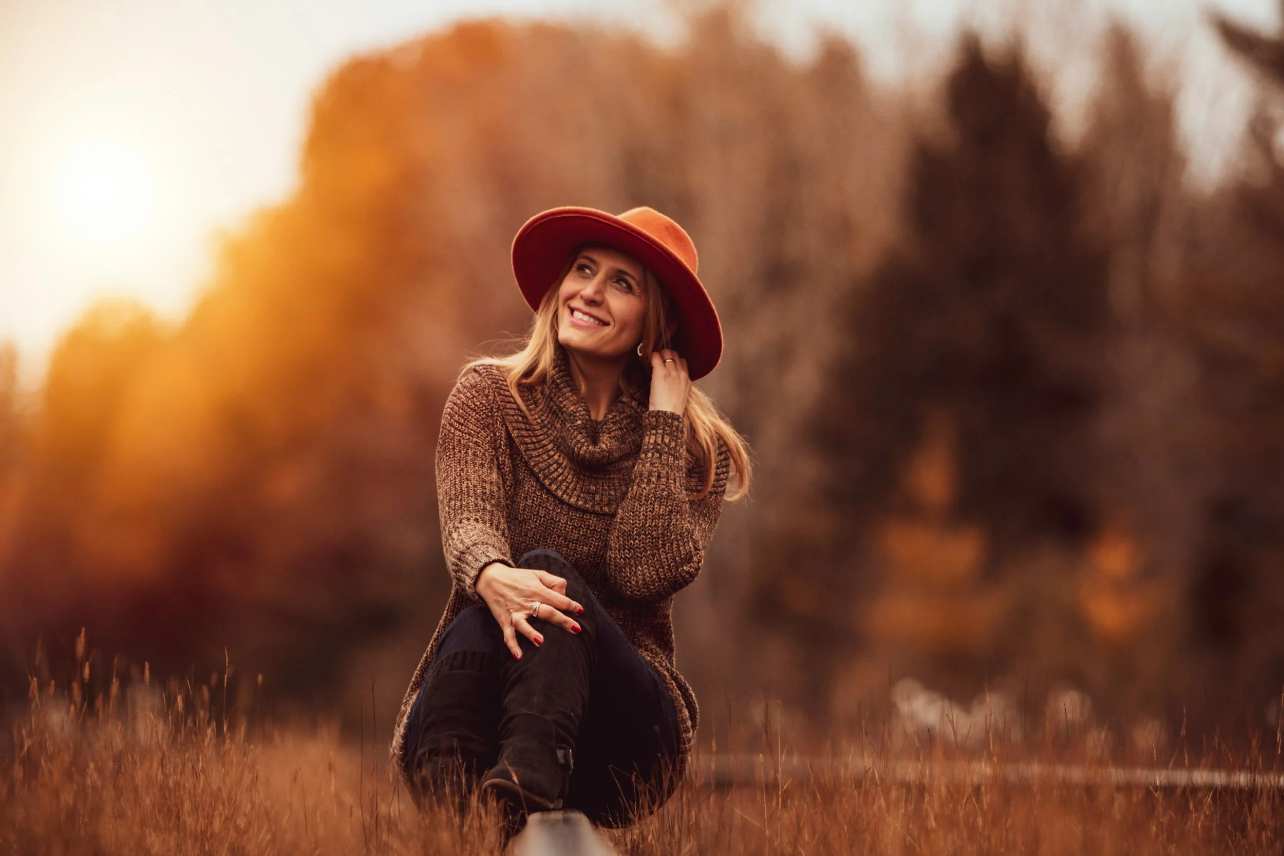 Middle aged woman sitting in a field at sunset wearing a wide brimmed hat and smiling, representing vitality and ease during the menopausal transition