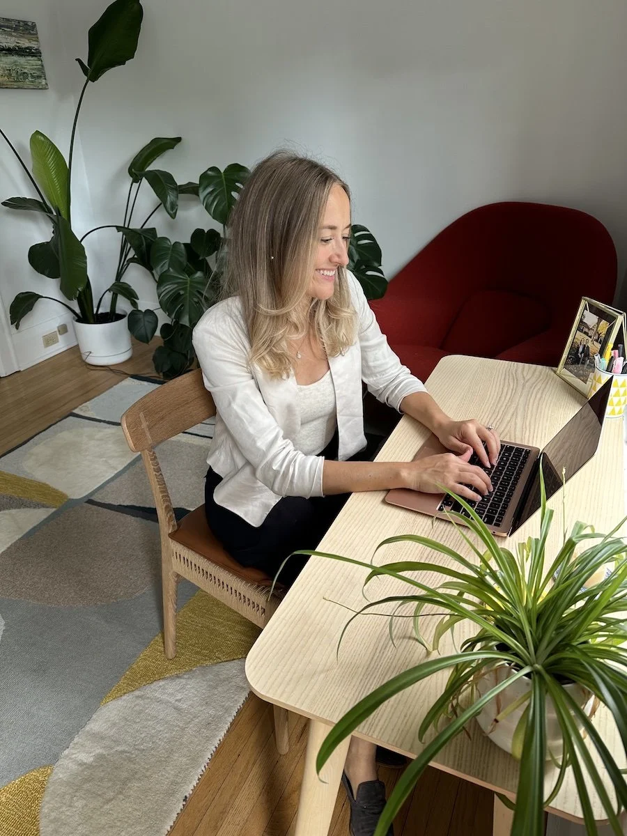 Nicole Argoma, integrative women's health nurse practitioner, smiling during a virtual consultation surrounded by plants in her office