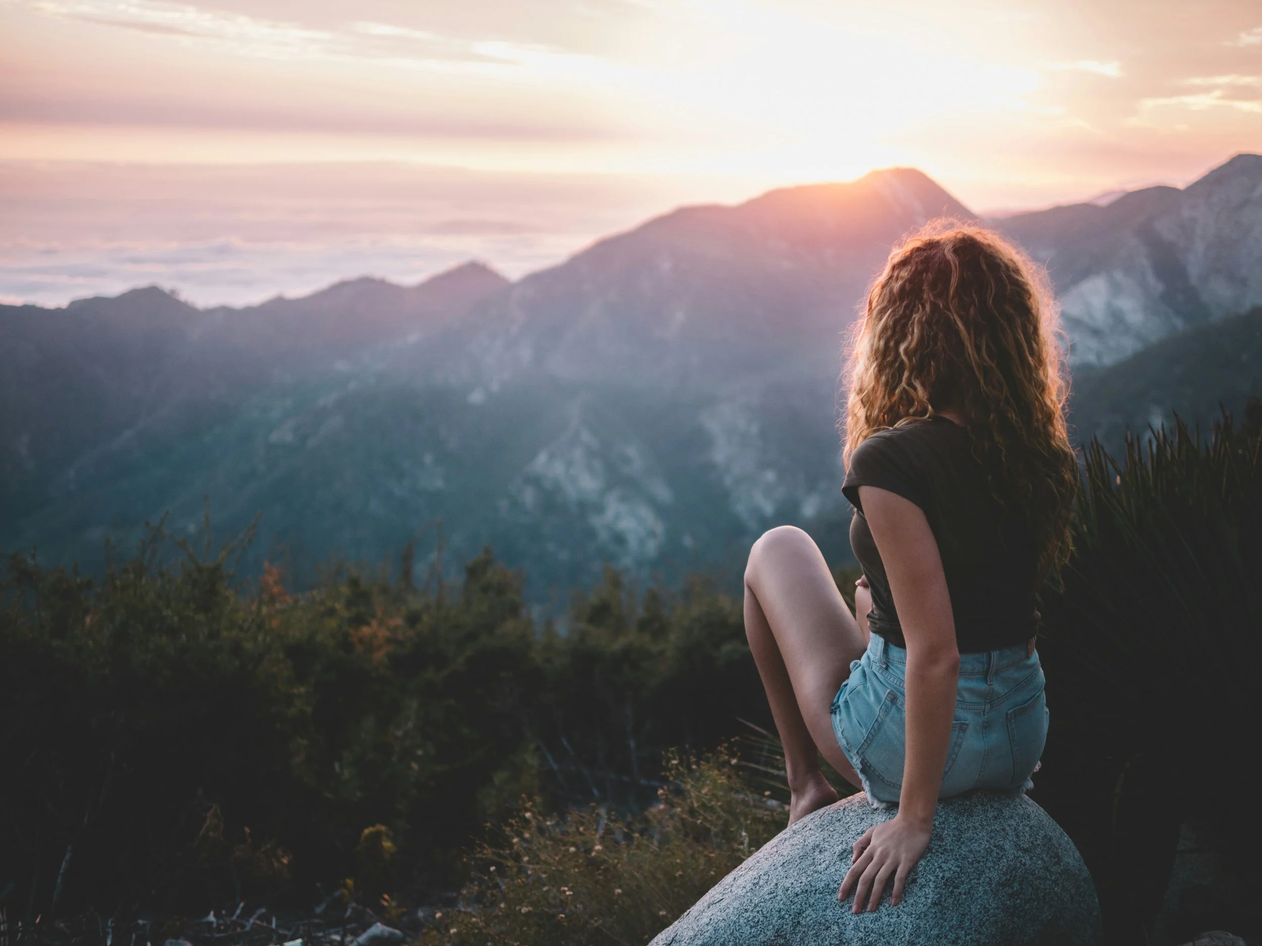 Woman sitting on a rock looking out at mountains in the distance representing strength, perspective and healing on the endometriosis journey