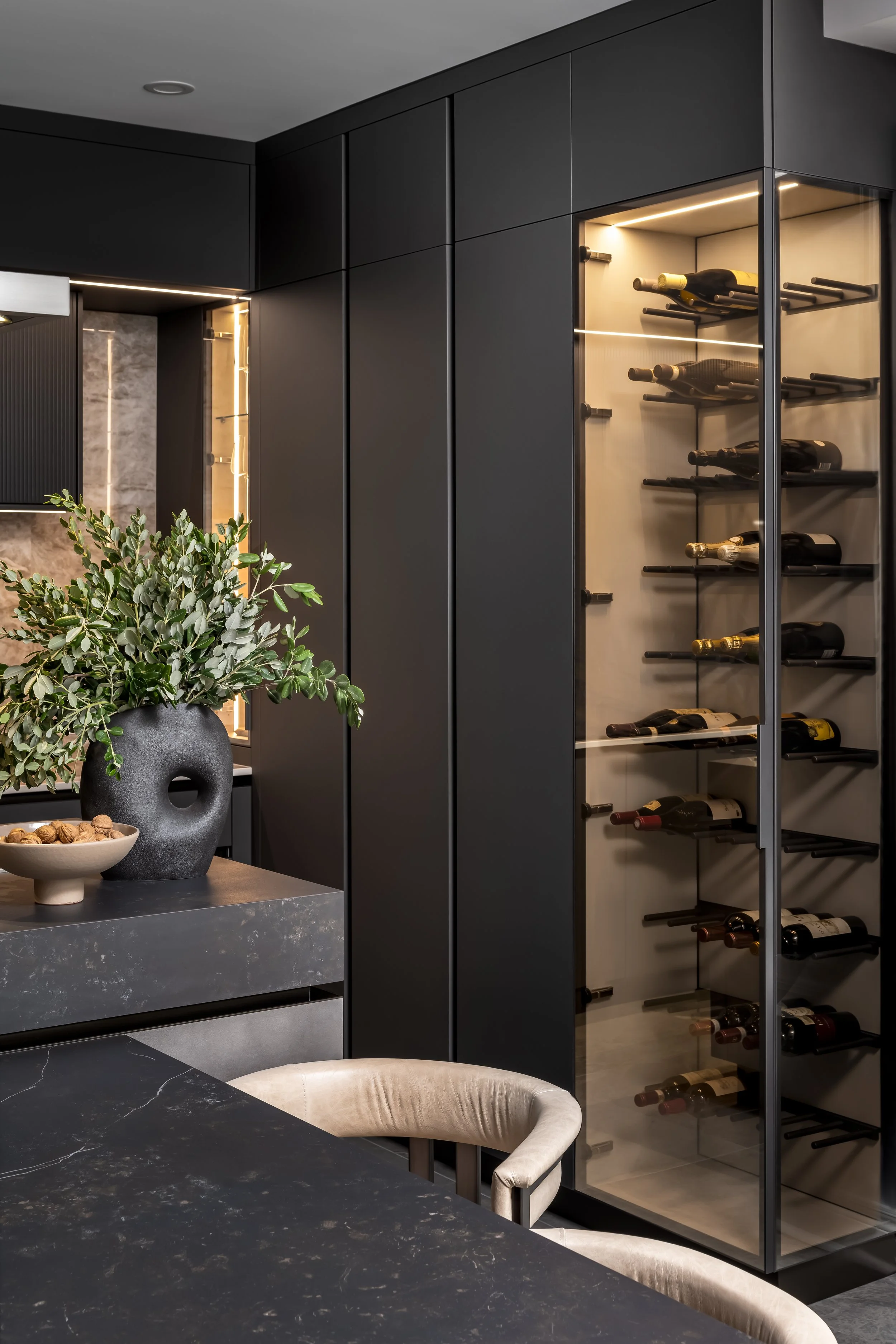 Modern kitchen with black cabinets and a wine storage cabinet with glass doors, wine bottles inside, and a plant in a black pot on the counter.