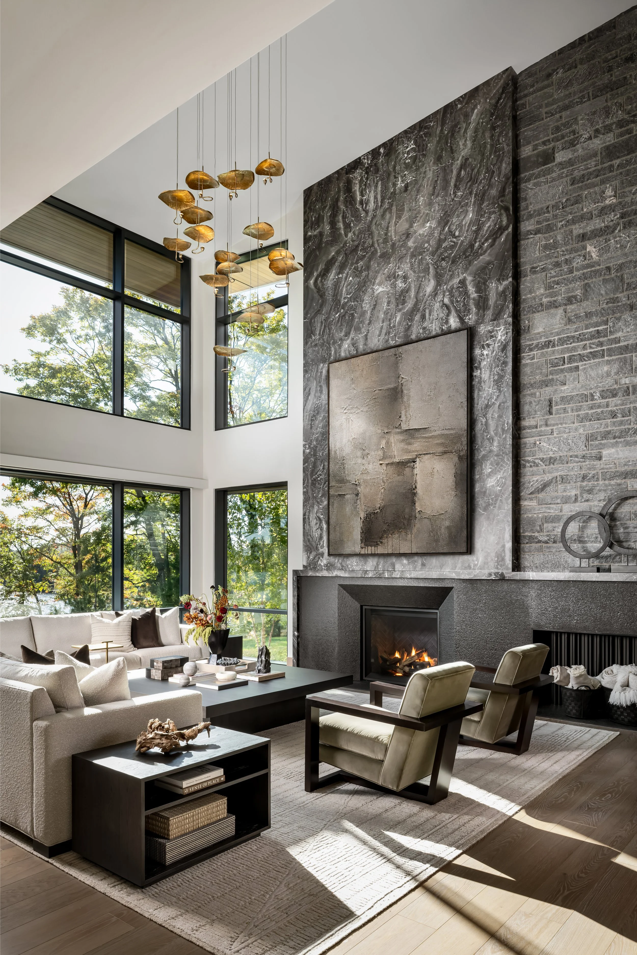 Modern living room with large windows, a fireplace, a marble wall, a beige sofa, armchairs, and a coffee table.