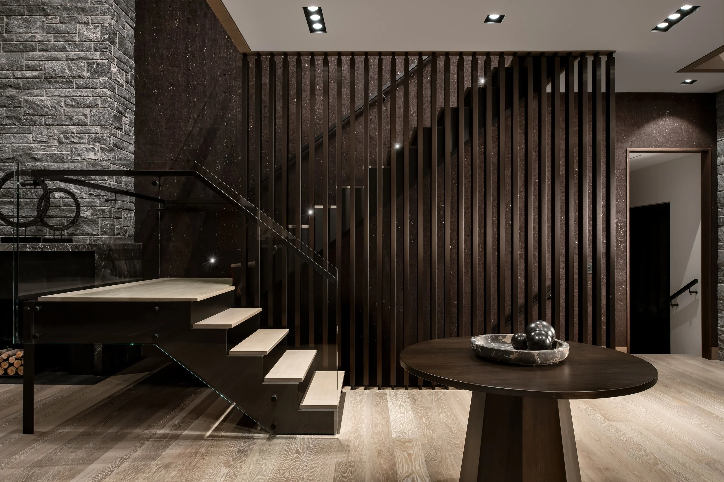 Modern interior with stone wall, wooden staircase, and decorative table with black and silver spheres.