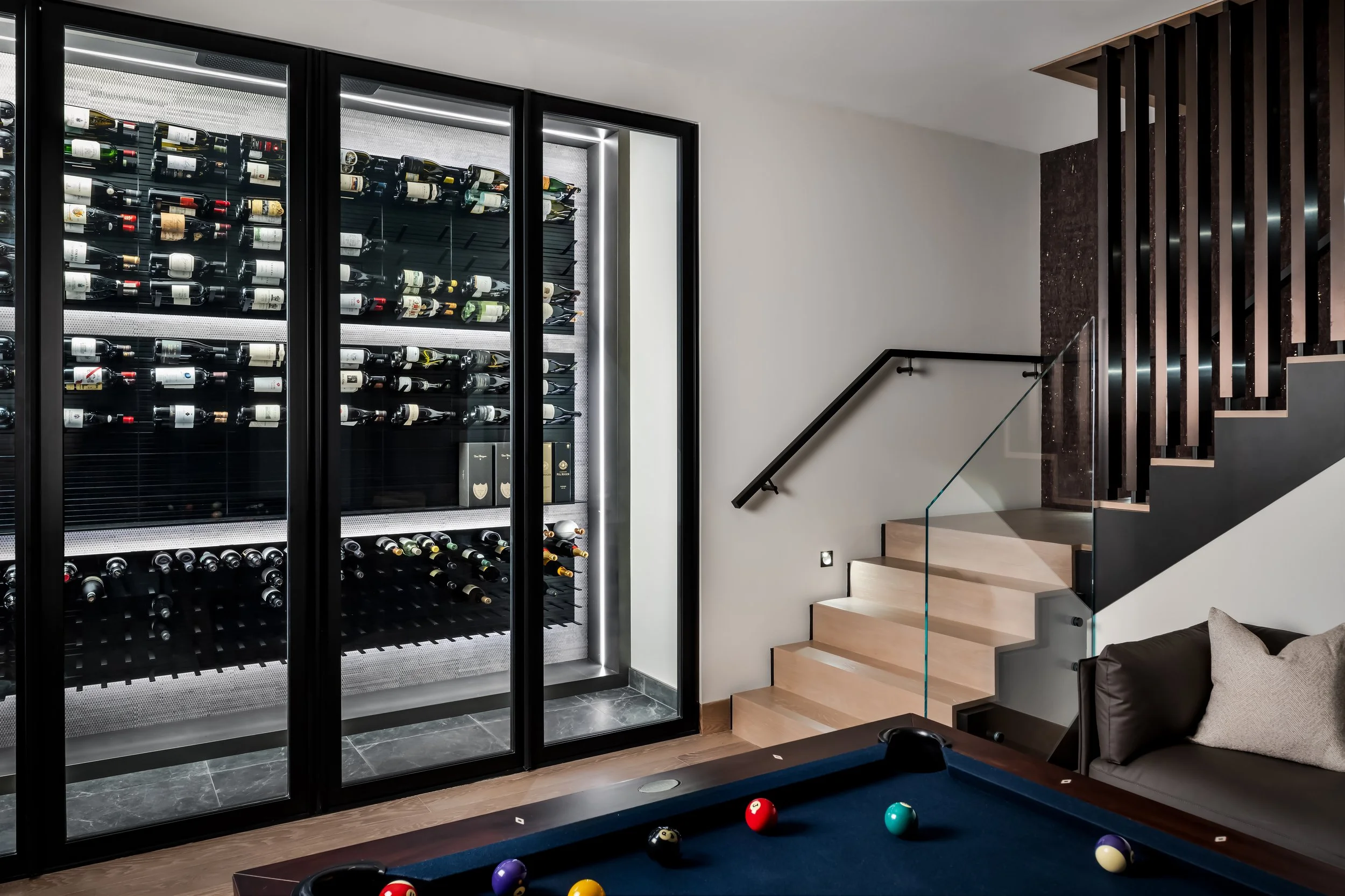 A modern interior room with a wine refrigerator, a staircase, and a pool table.