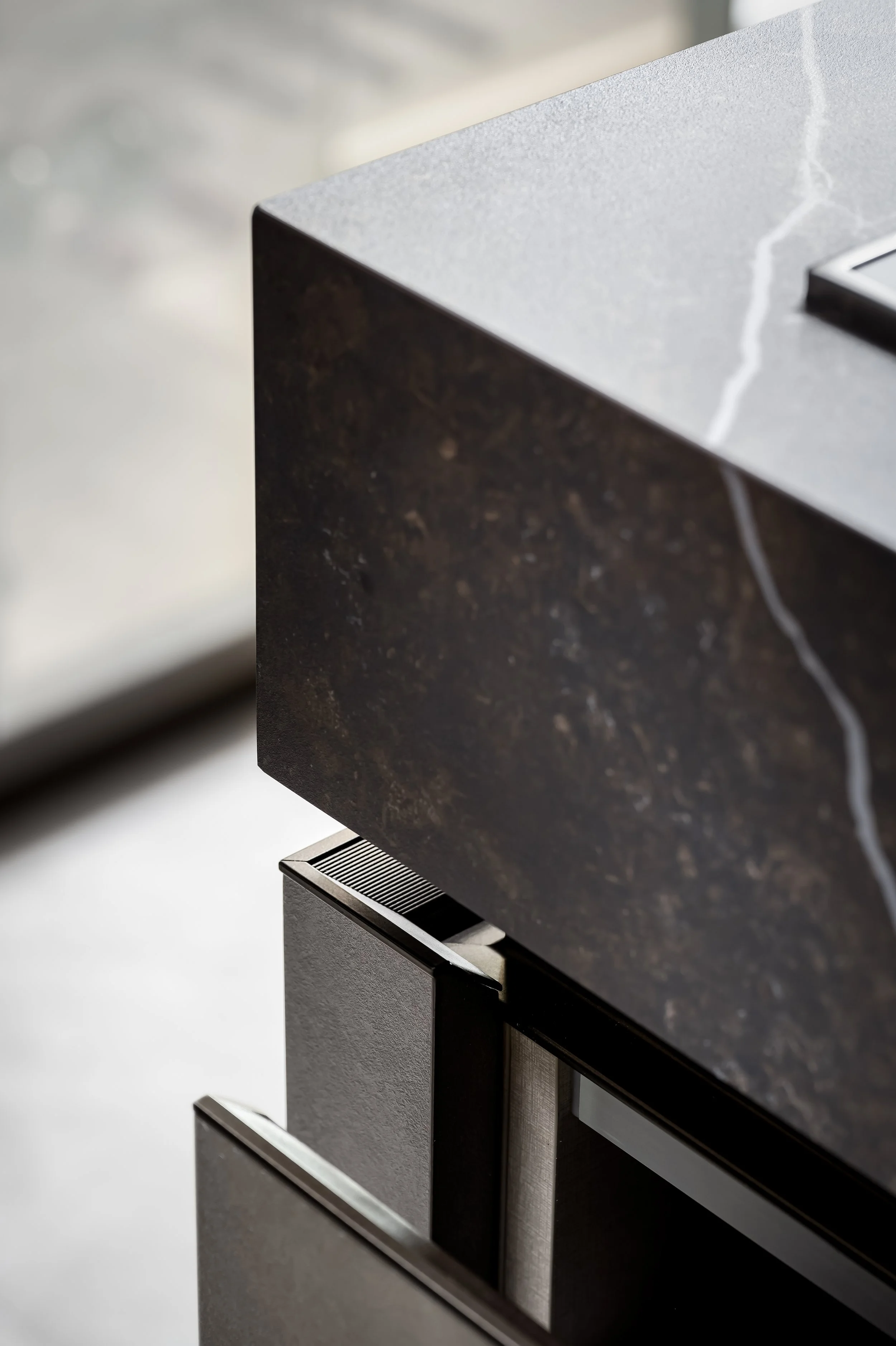 Close-up of a black granite kitchen countertop with a white marble pattern, above a black kitchen appliance with a vented top.