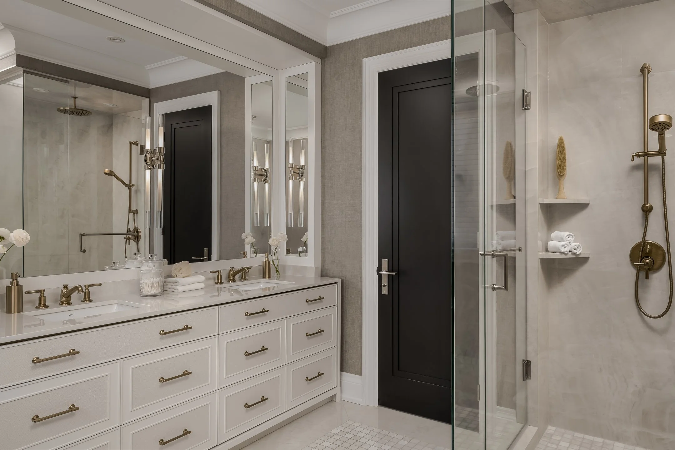 Modern bathroom with white vanity, gold fixtures, large mirror, and walk-in shower with gold shower fixtures and glass enclosure.