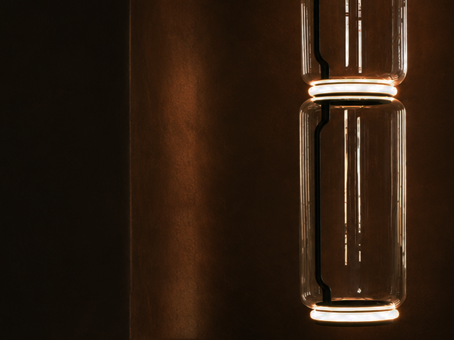 Close-up of a modern, cylindrical LED light fixture mounted on a dark brown wall, illuminating with a warm glow.