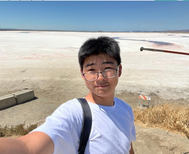 Person with long hair making a peace sign in front of colorful art on a wall.