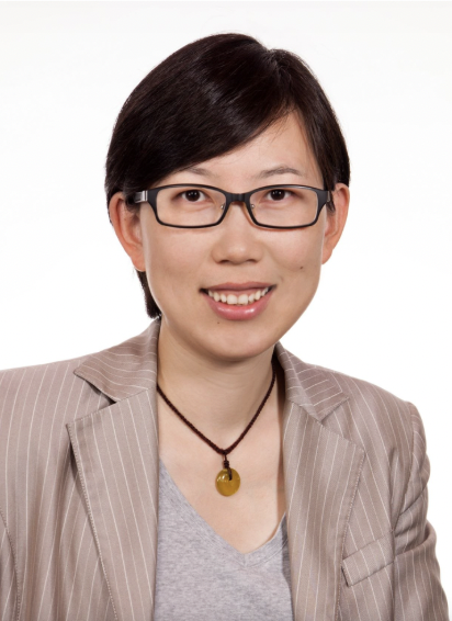 A woman wearing glasses, a beige pinstripe blazer, and a gray shirt, smiling at the camera against a white background.