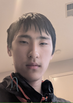 A young man with short black hair and light skin taking a selfie indoors, wearing a black jacket with a red zipper.