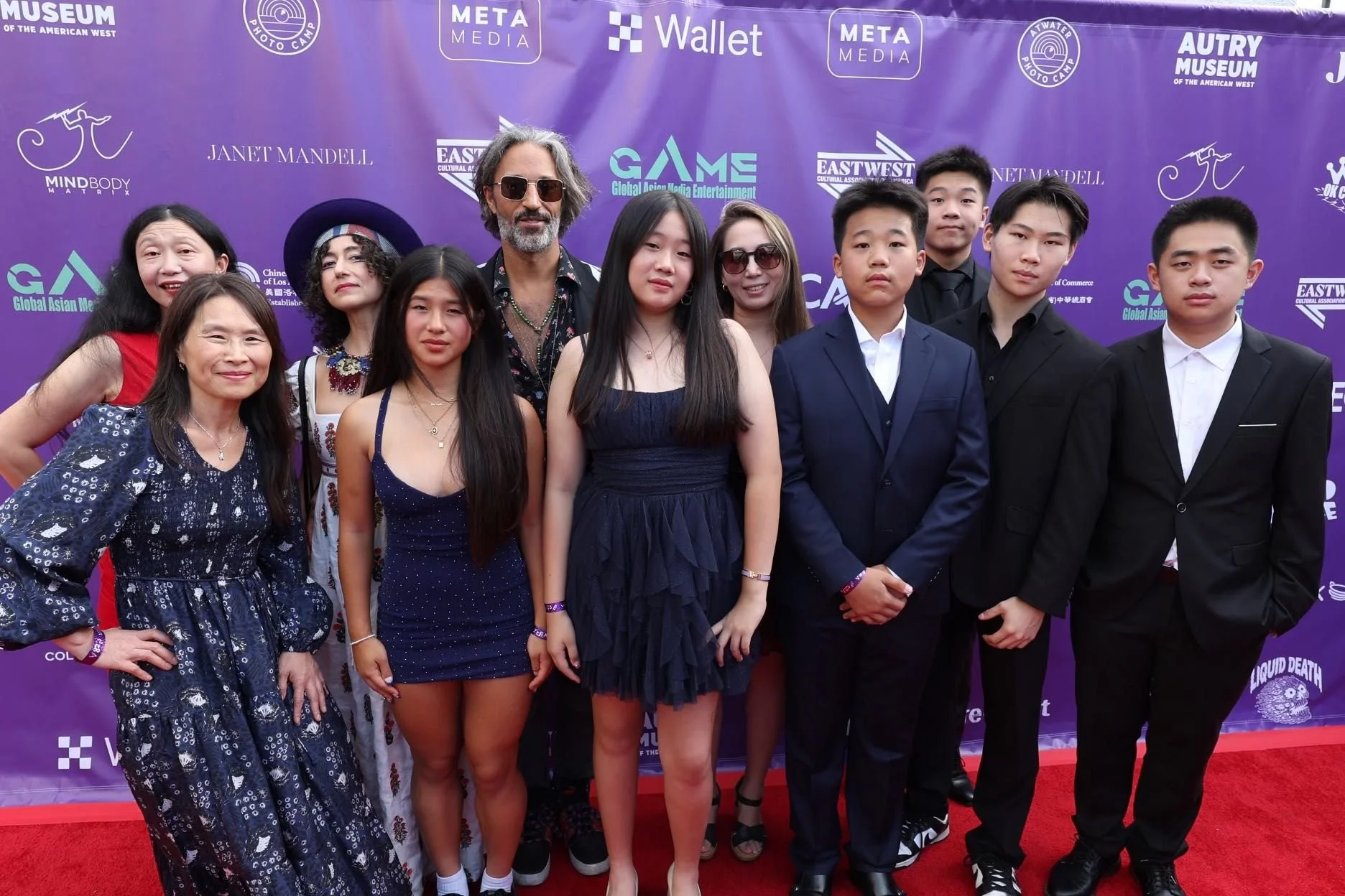 Group of people posing on a red carpet with a purple backdrop, logos of various sponsors visible.