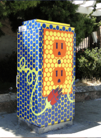 A utility box painted with a colorful design of electrical outlets and a plug over a honeycomb pattern.