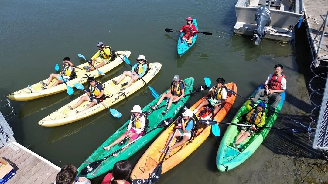 Group of people kayaking in colorful kayaks on calm water near a dock.
