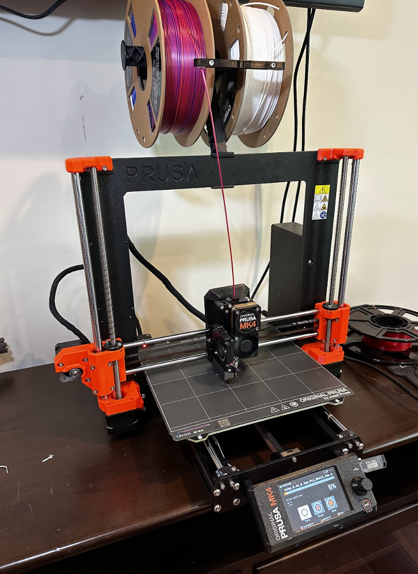 Prusa MK4 3D printer with dual filament spools, one pink and one white, on a tabletop.