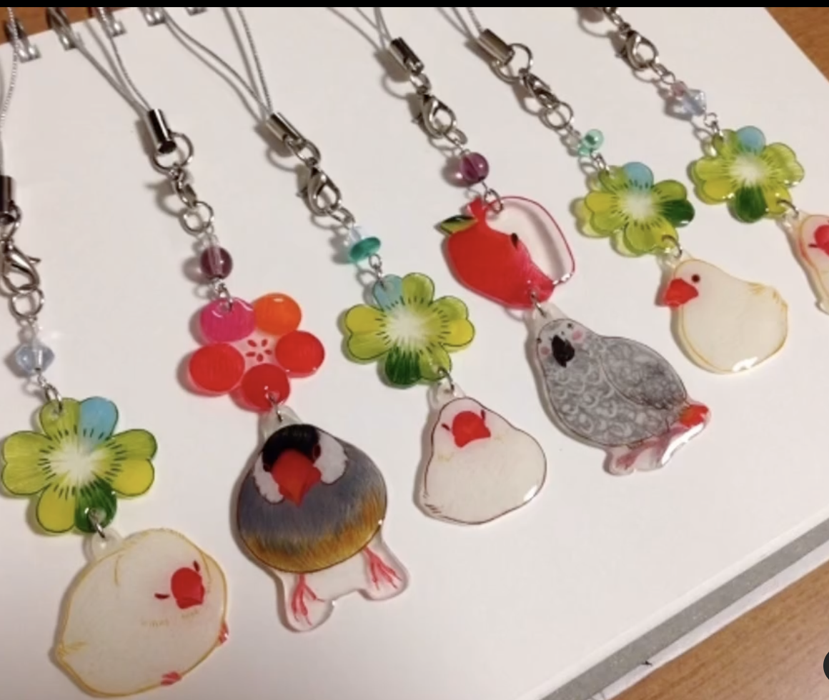 Colorful bird-themed keychain charms with flower decorations on a white background.